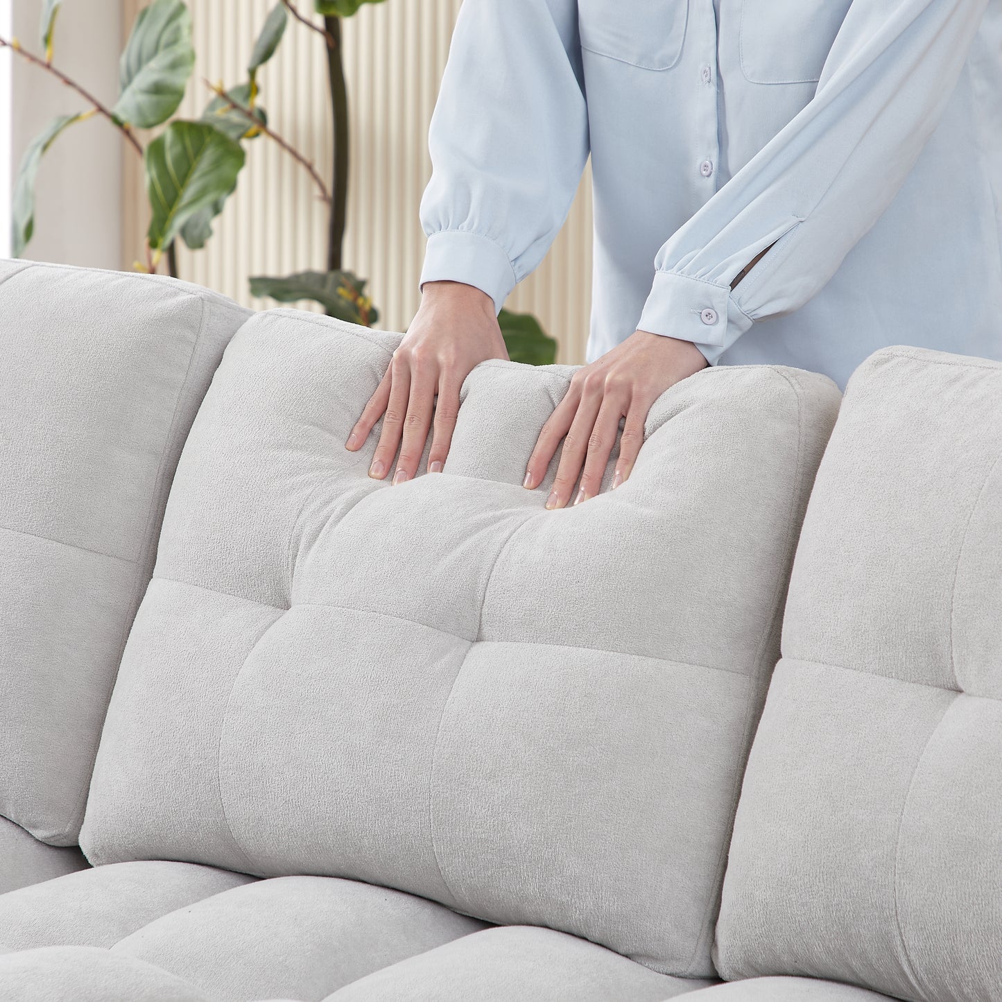 Plush light gray boucle fabric sofa with deep tufted cushions hands adjusting a pillow