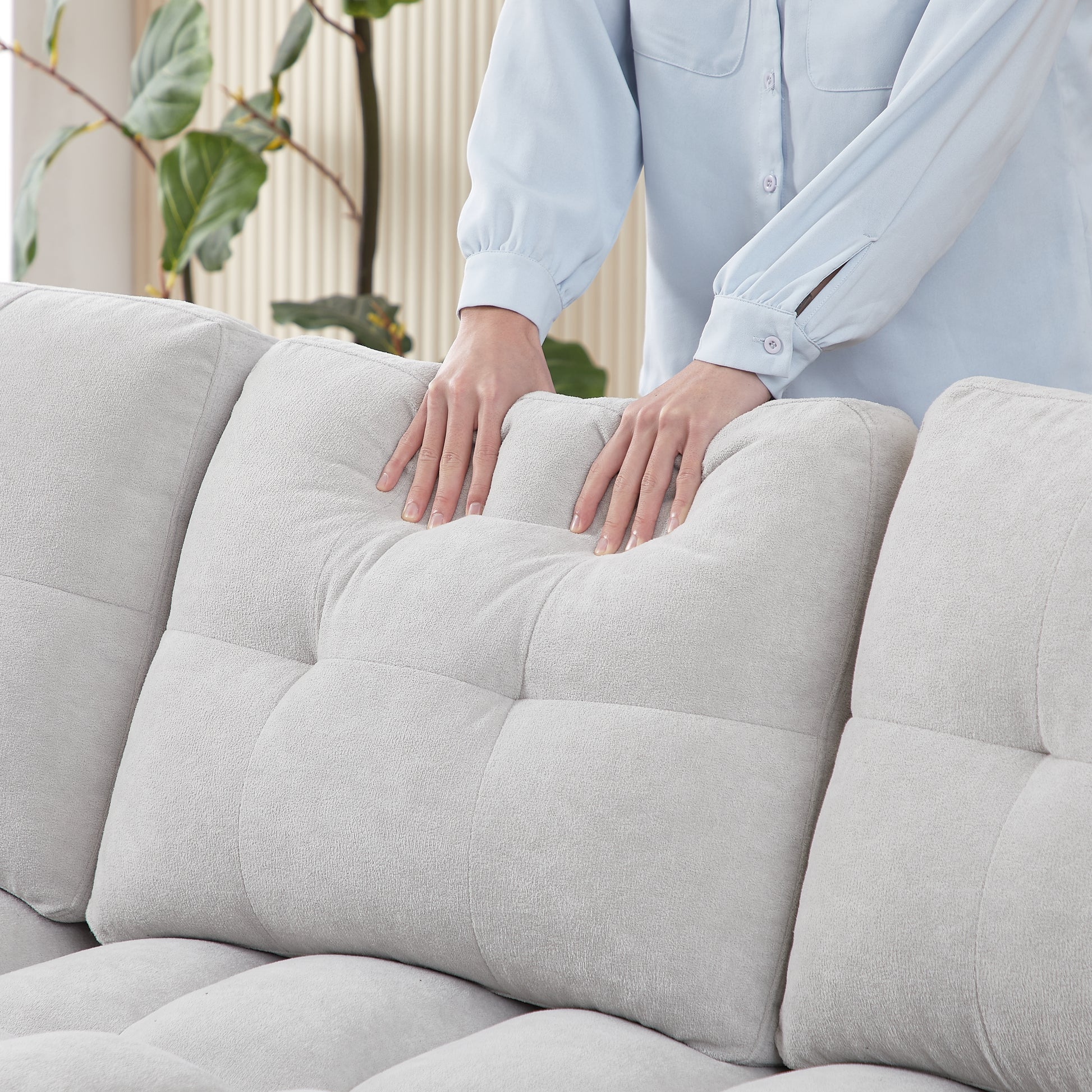 Plush light gray boucle fabric sofa with deep tufted cushions hands adjusting a pillow