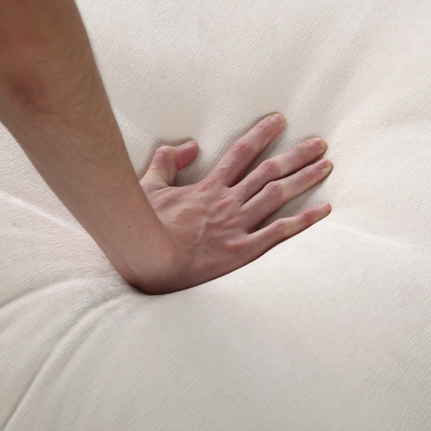 Hand pressing into plush beige mattress for comfort testing