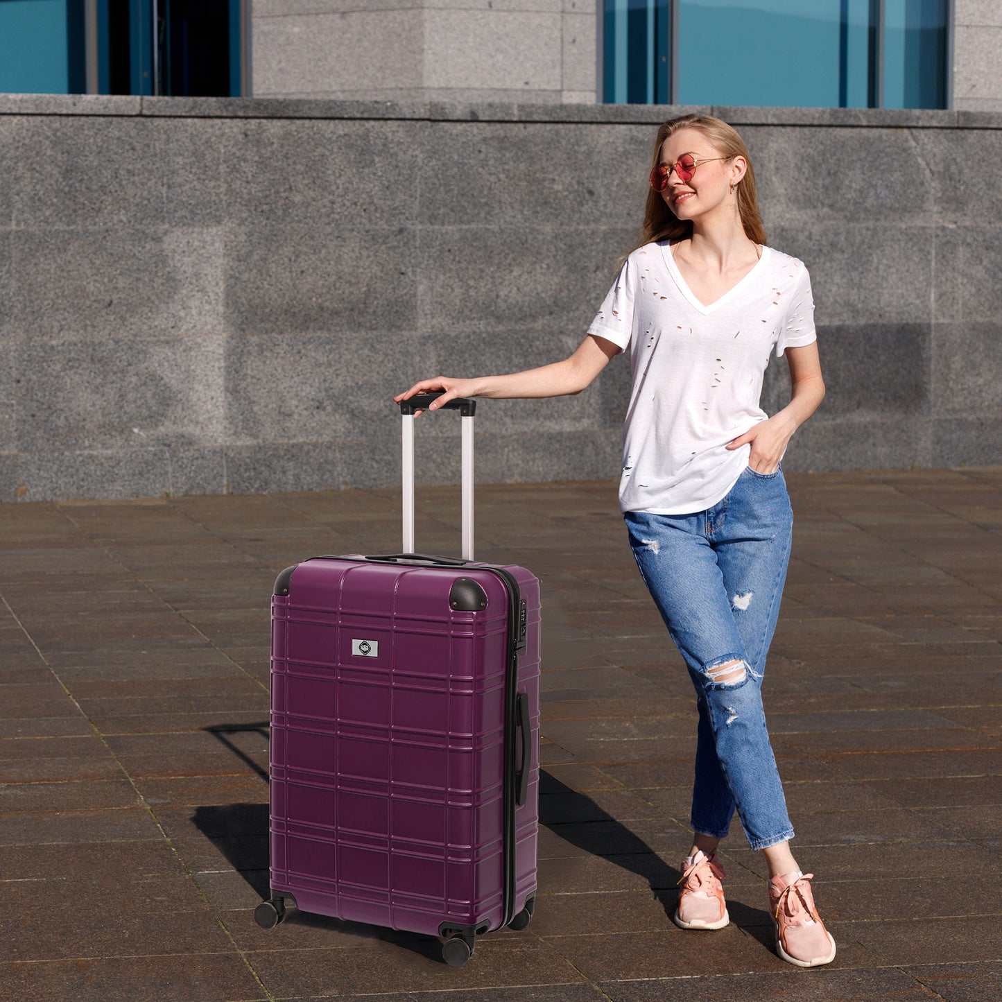 A stylish woman with ripped jeans holds the handle of a deep purple hardshell suitcase