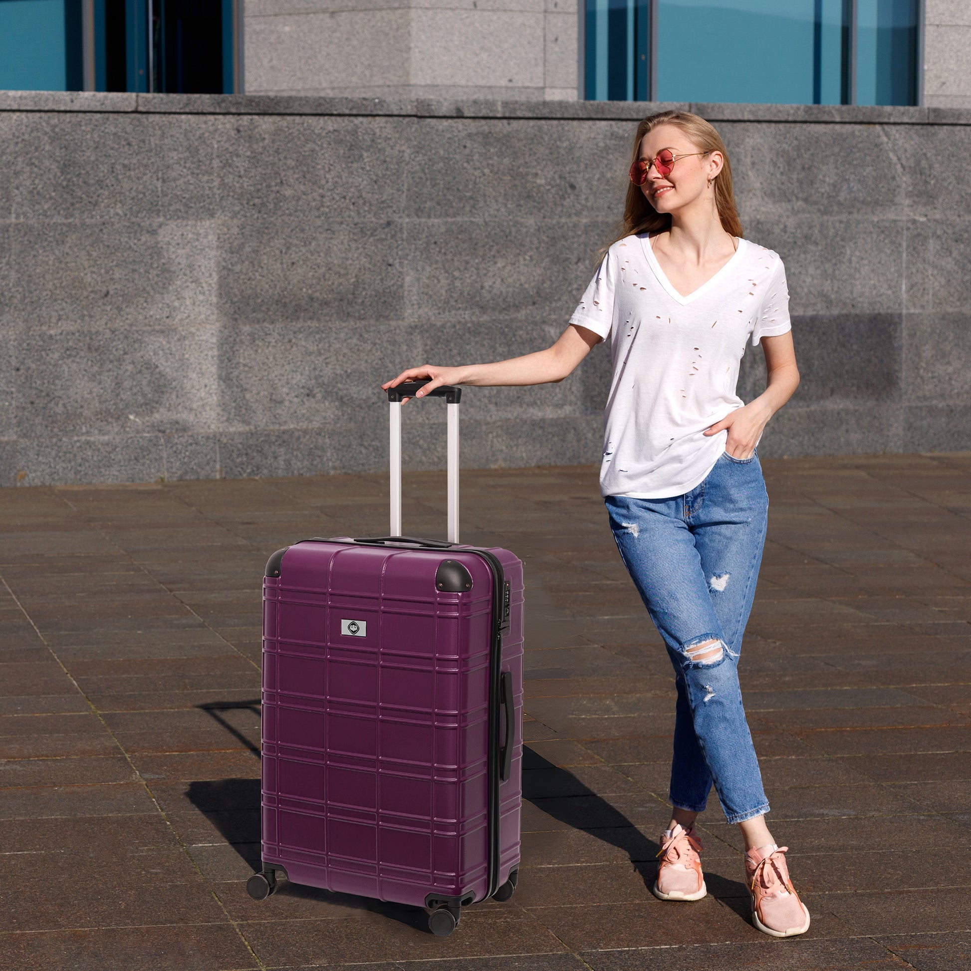 A stylish woman with ripped jeans holds the handle of a deep purple hardshell suitcase