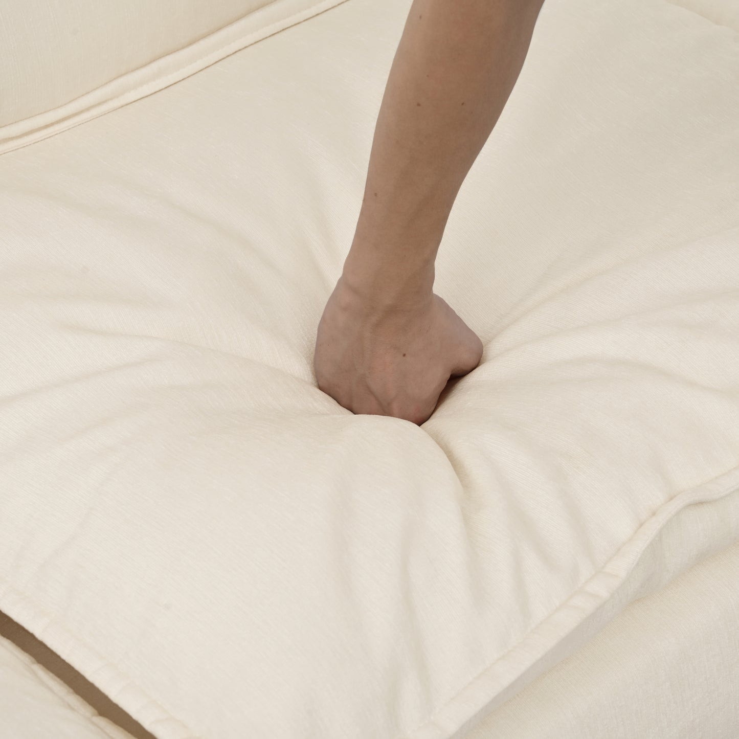 Hand pressing into soft cream linen sofa cushion for comfort test