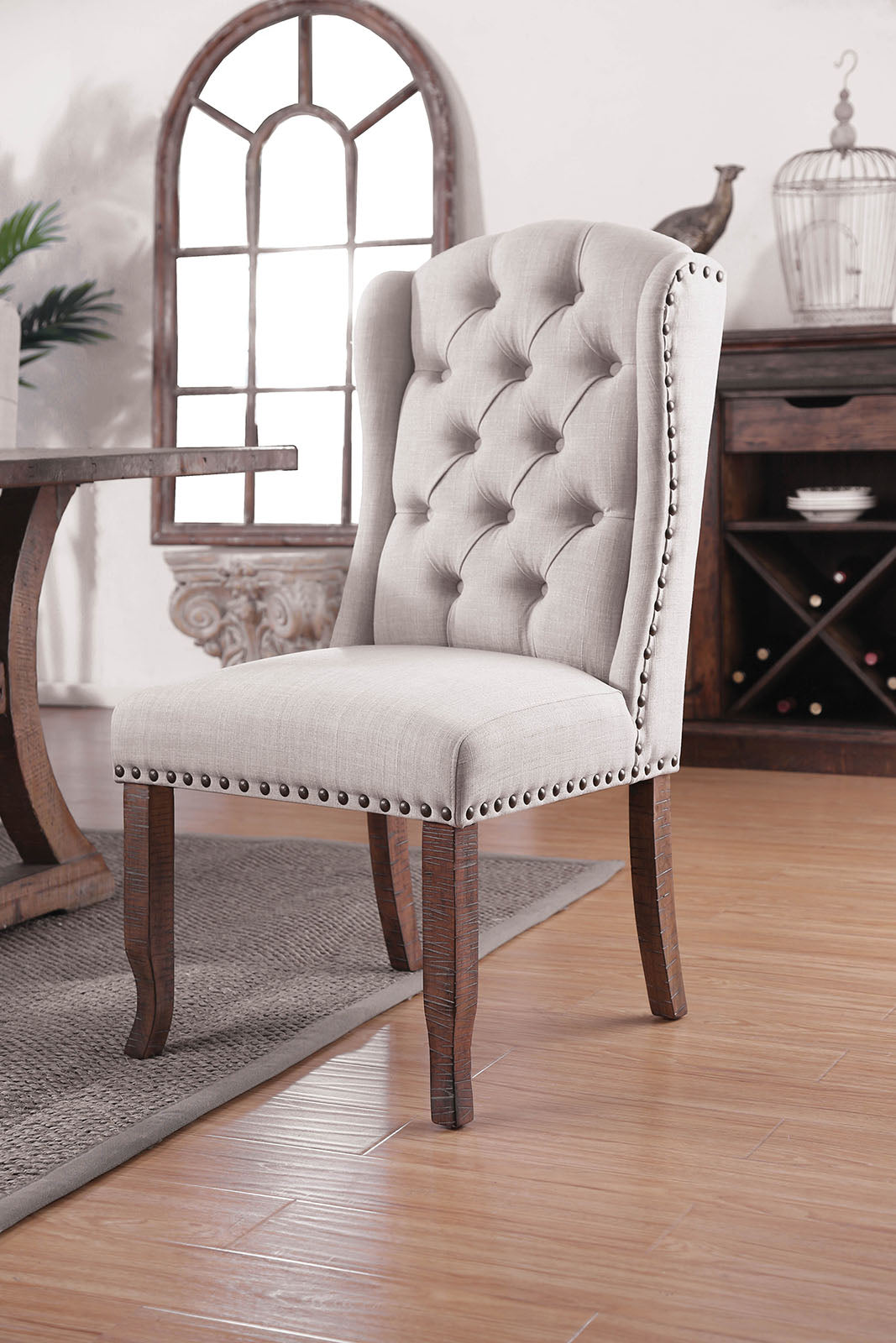 Tufted wingback dining chair in light gray linen with nailhead trim and dark wood legs
