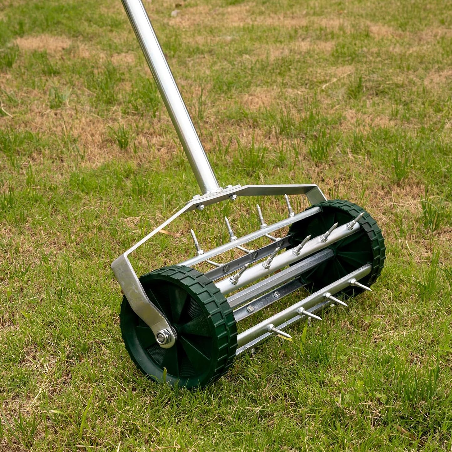Garden lawn aerator with metal spikes and green wheels on grass