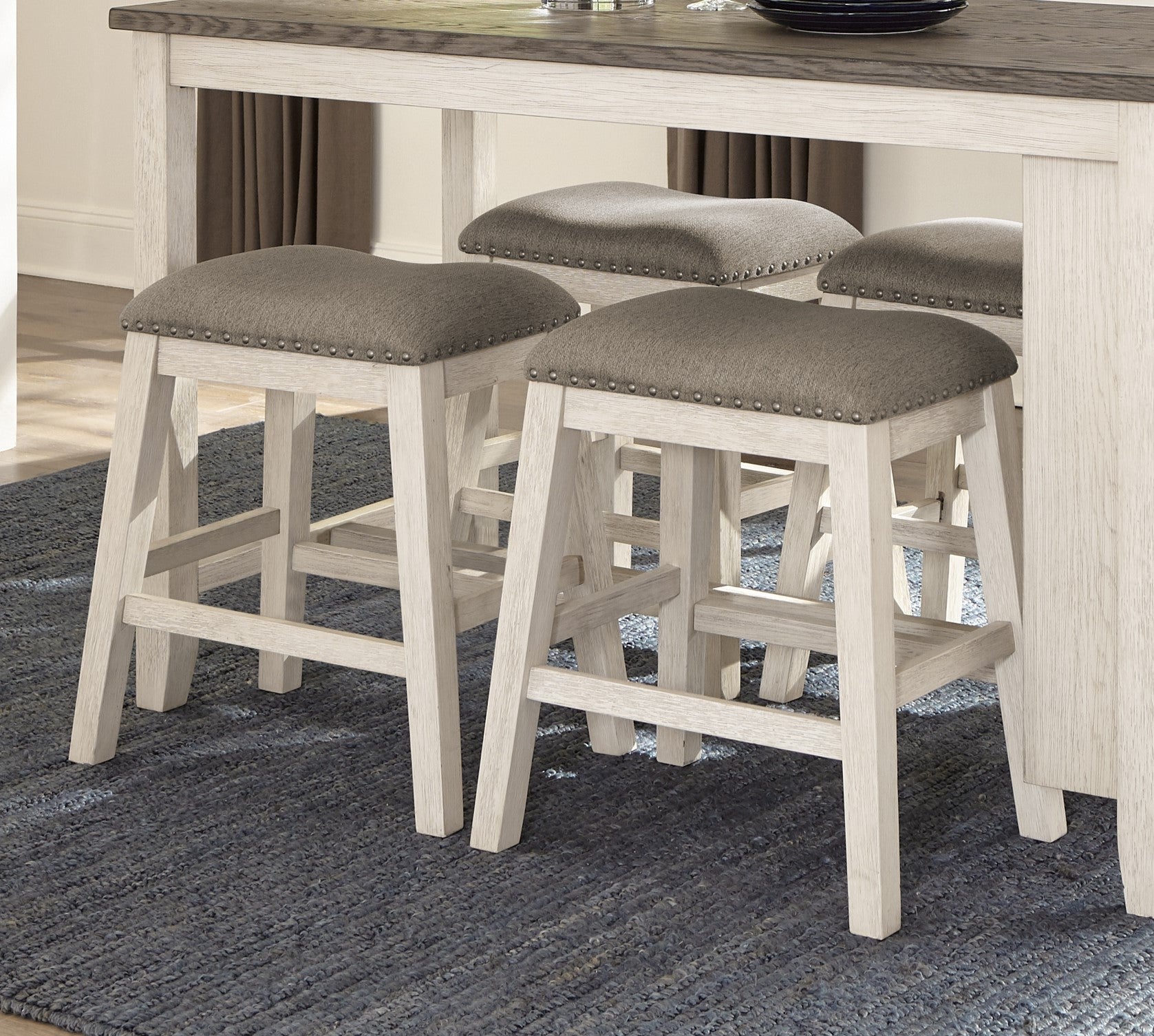 Gray upholstered counter stools with nailhead trim and distressed wood legs