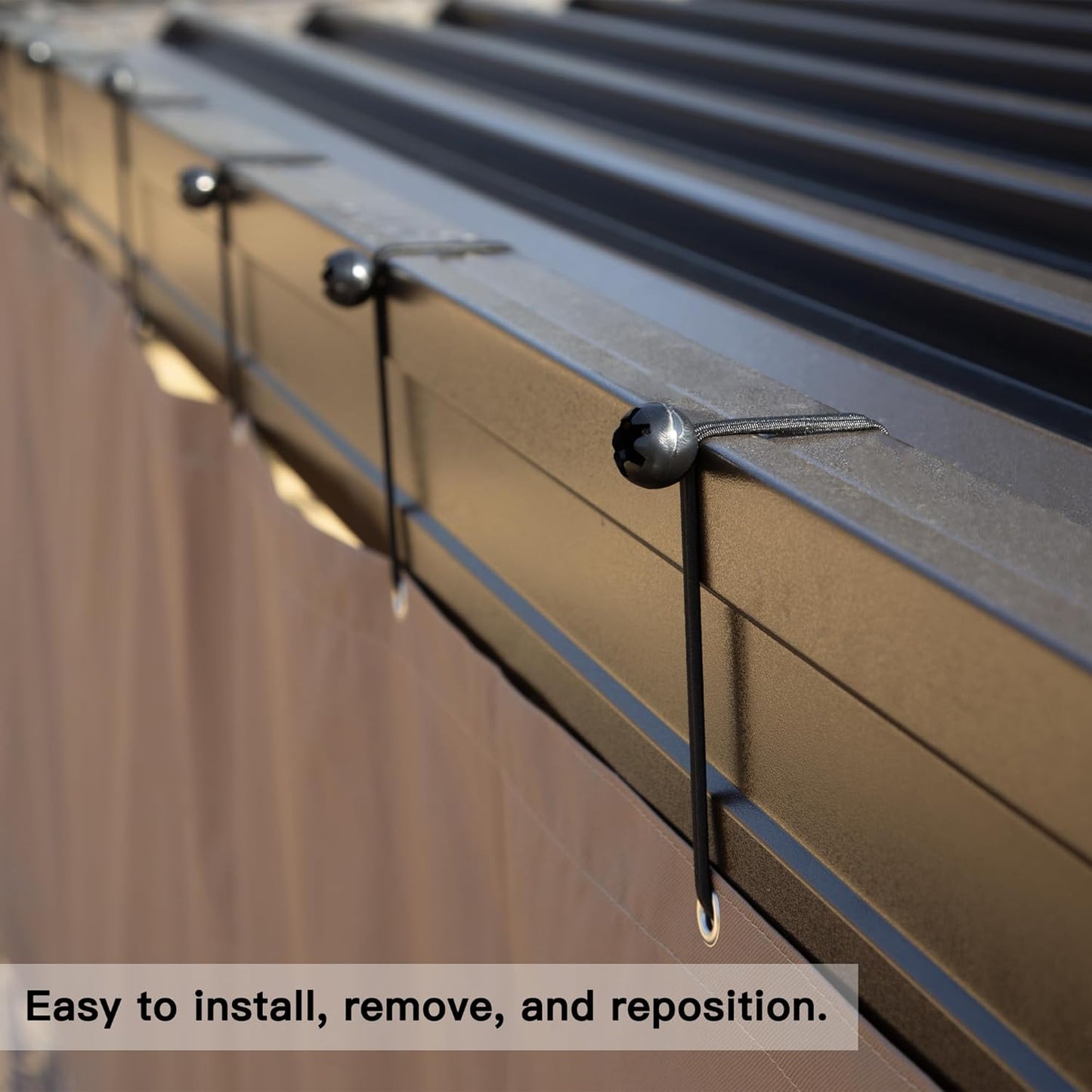 Closeup of brown metal roof panels secured by black bungee cords with ball ends and grommets