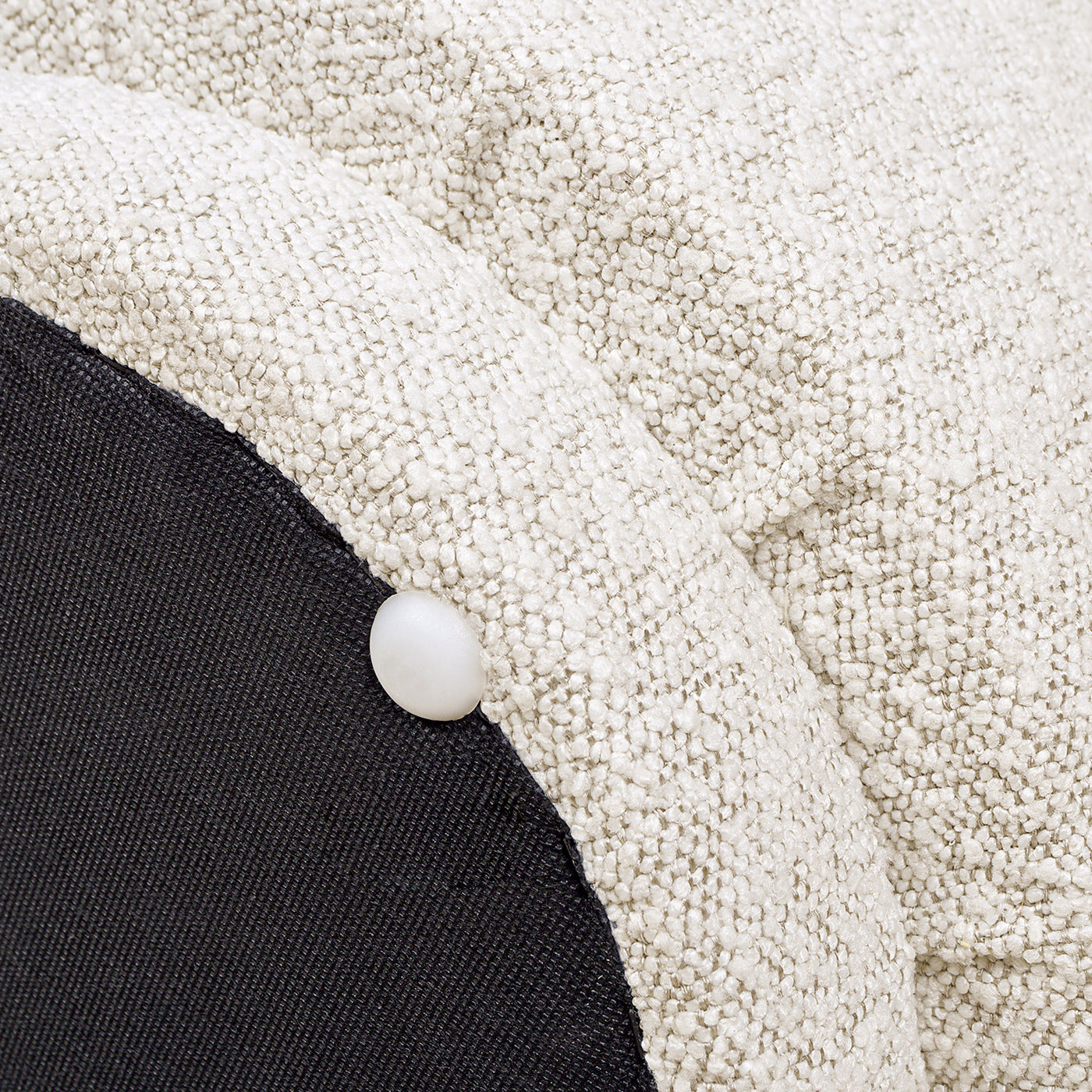 Closeup of textured cream boucle fabric on a sofa with a dark grey underside panel and decorative button