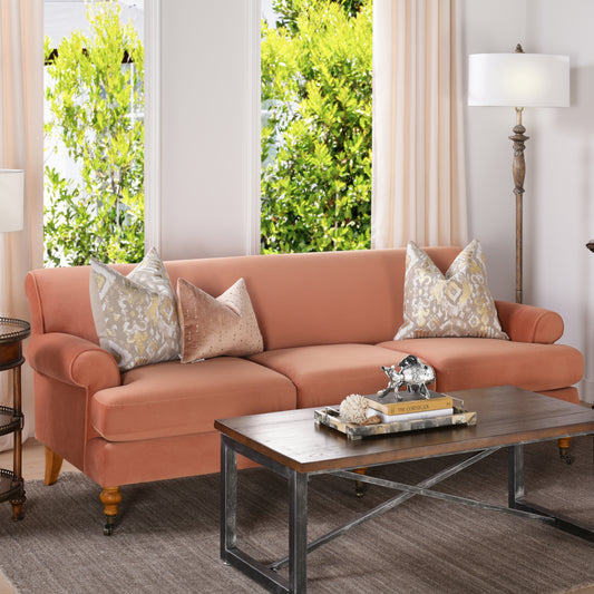 Elegant coral velvet sofa with detailed patterned throw pillows and a tufted seat
