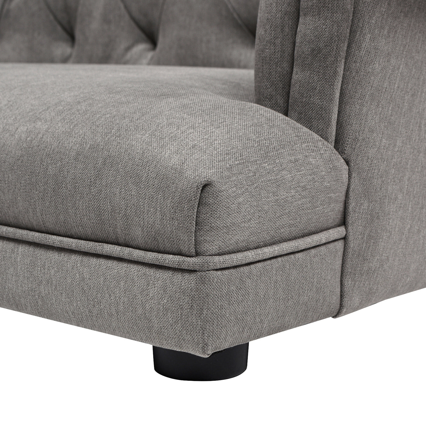 Closeup of a grey tufted sofa armrest with a black leg