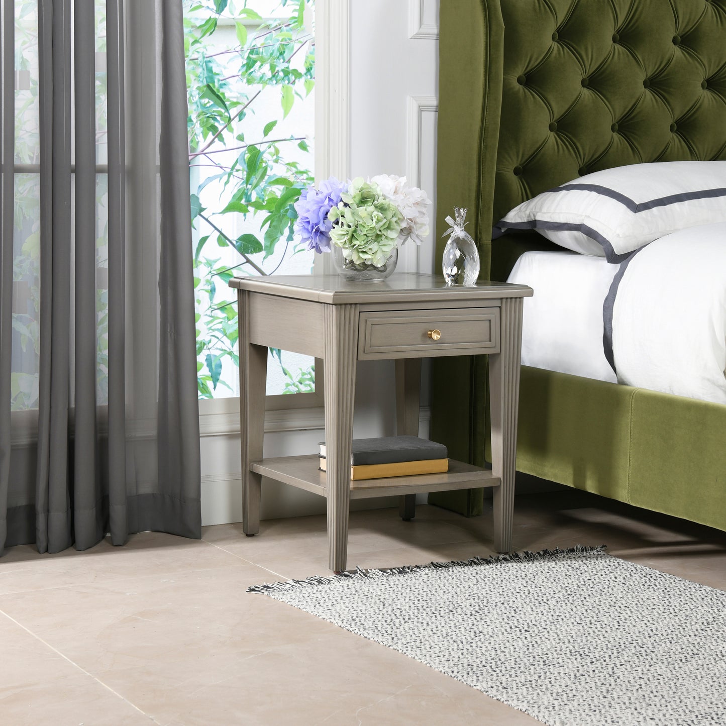 Grey wooden end table with brass knob drawer and shelf flanking a bed