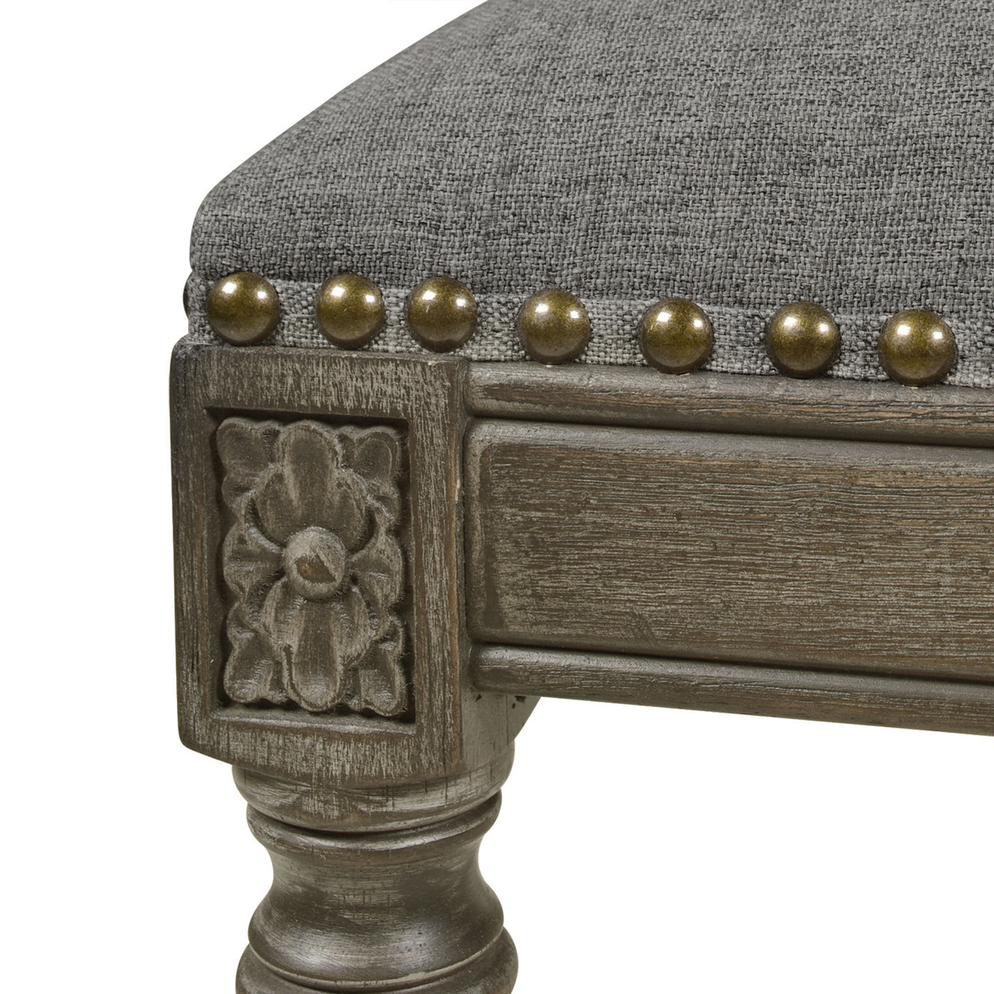 Closeup of a grey upholstered accent chair leg with carved detail and brass nailheads