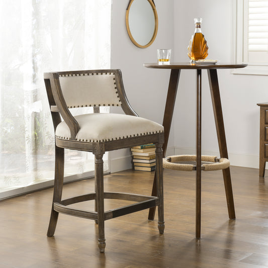 Rustic grey wooden bar stool with beige upholstered seat and nailhead trim