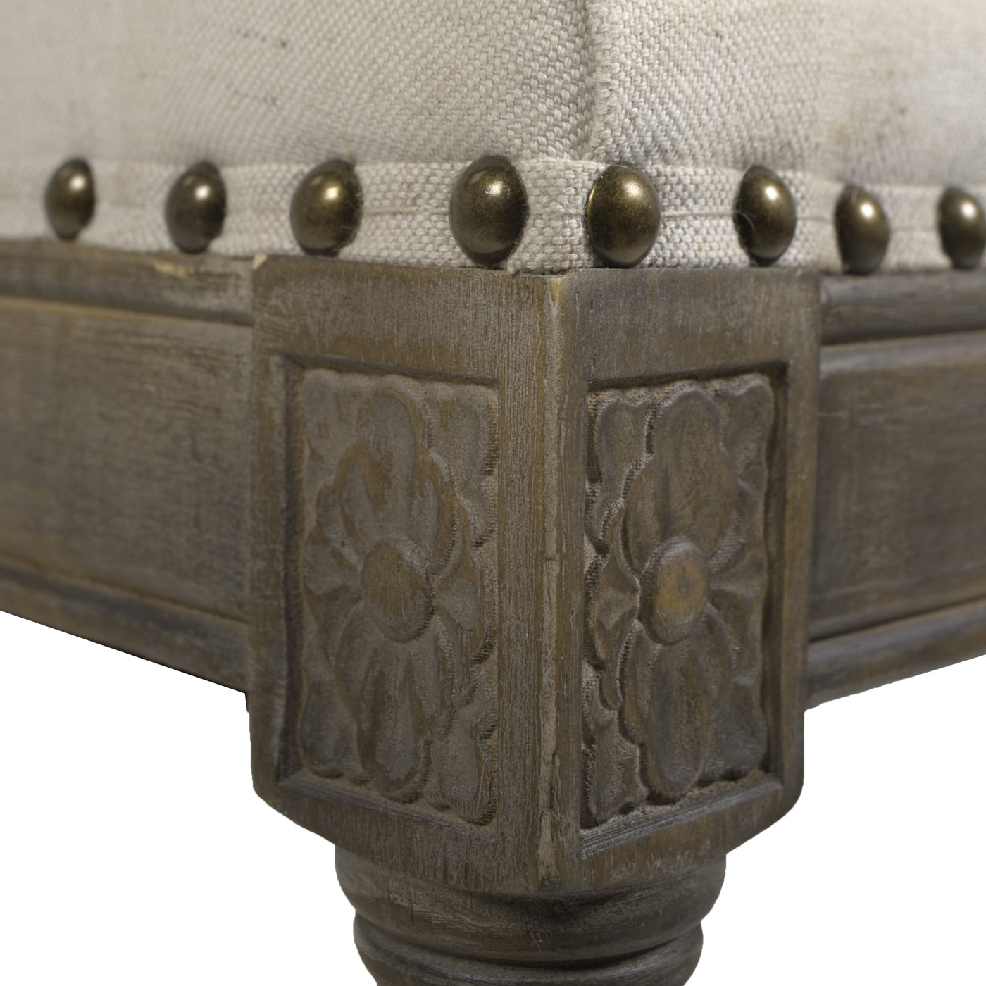 Ornate carved wooden table leg with antique brass nailhead trim on light beige fabric upholstery