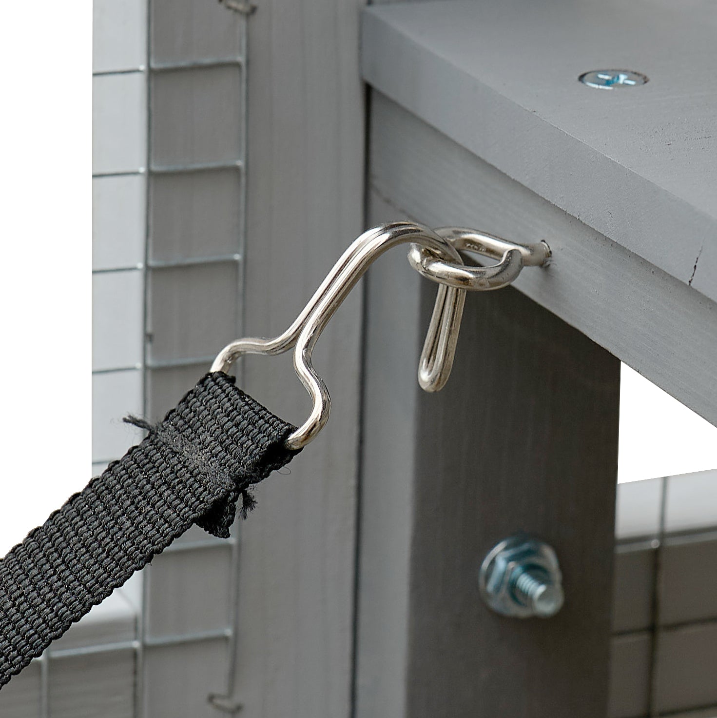 Closeup of a grey wooden chicken coop with a metal hook and black strap for secure enclosure