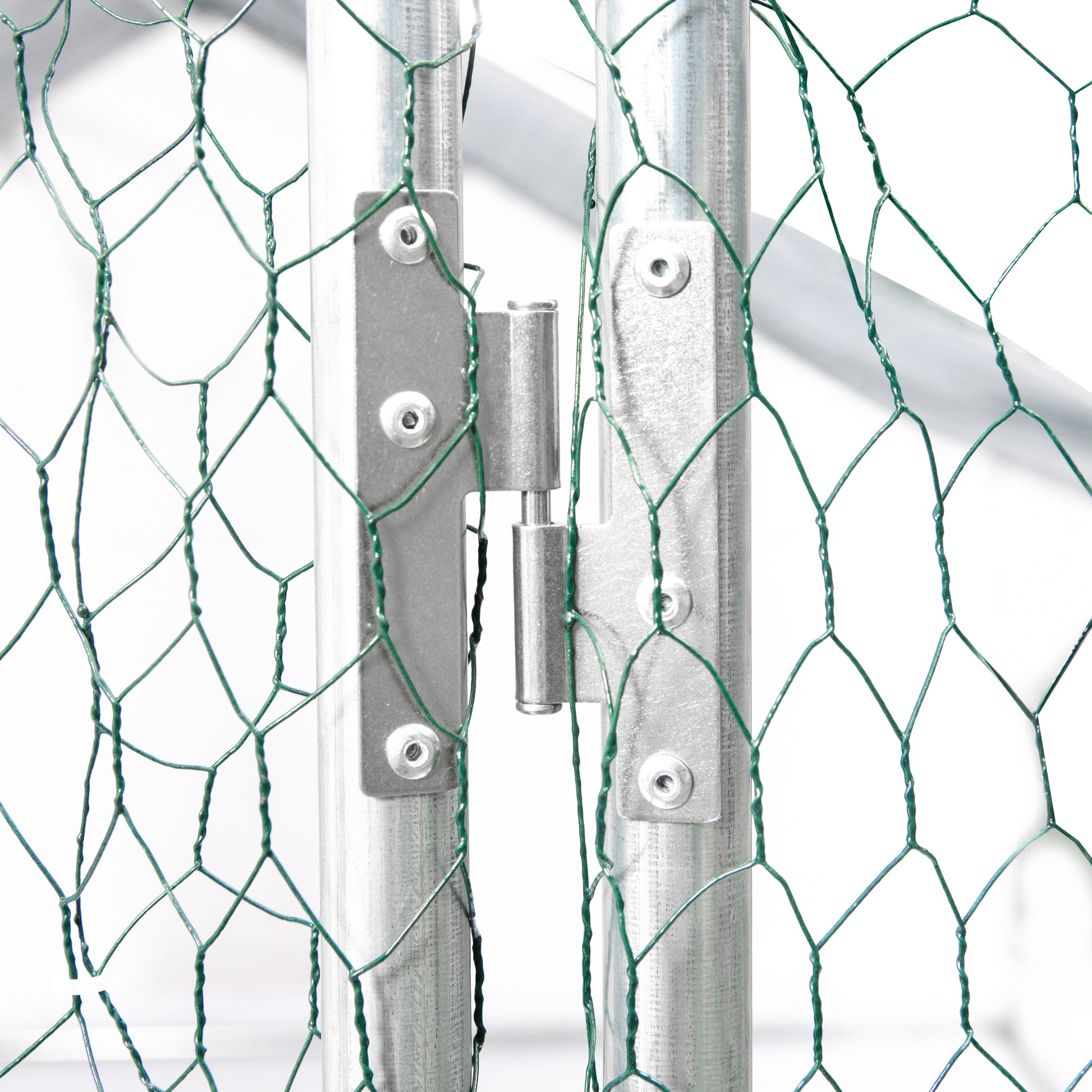 Closeup of a galvanized steel gate hinge connecting two vertical posts with green wire mesh visible