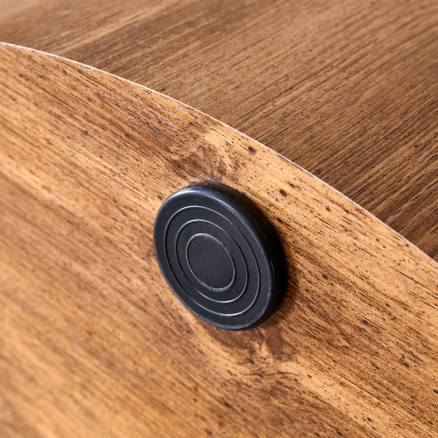 Closeup of a black circular furniture foot with concentric rings on a woodgrain laminate surface