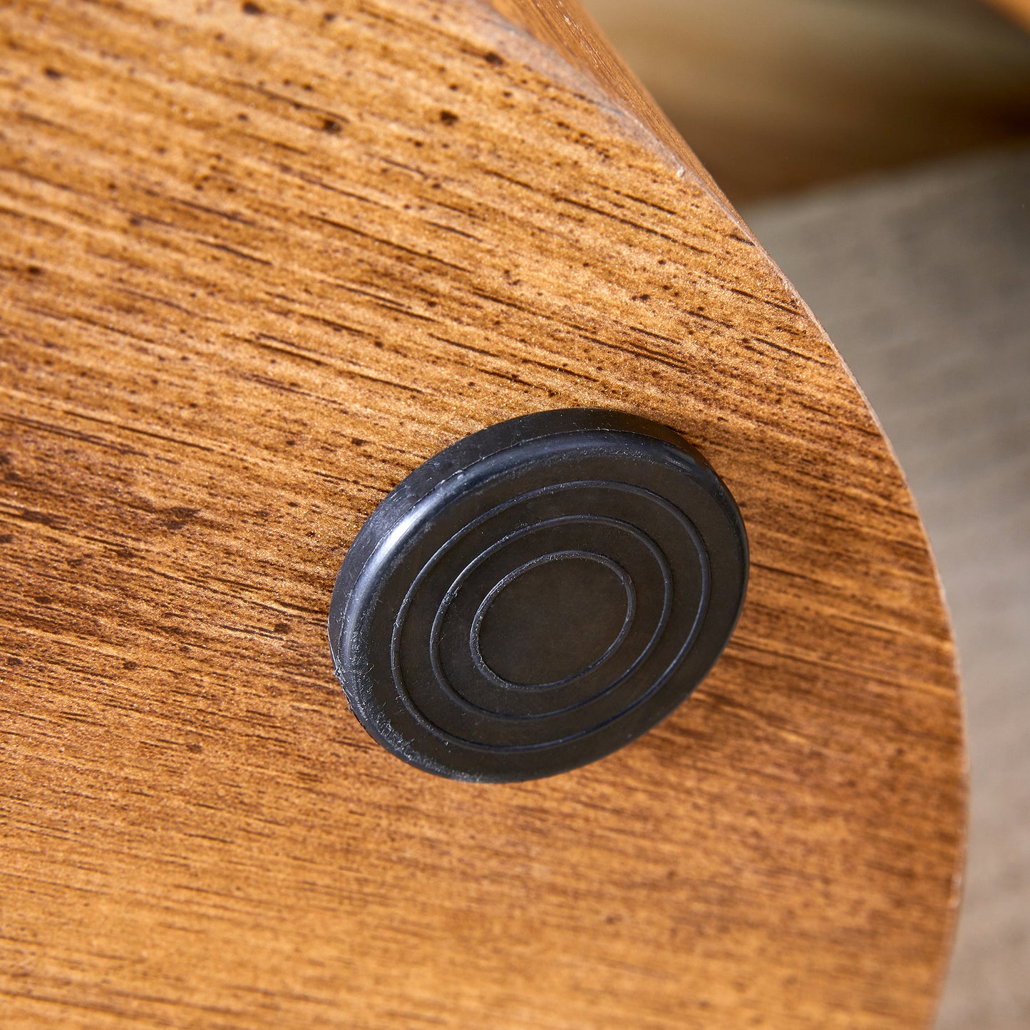 Closeup of a round black rubber foot with concentric circles on a textured wooden surface