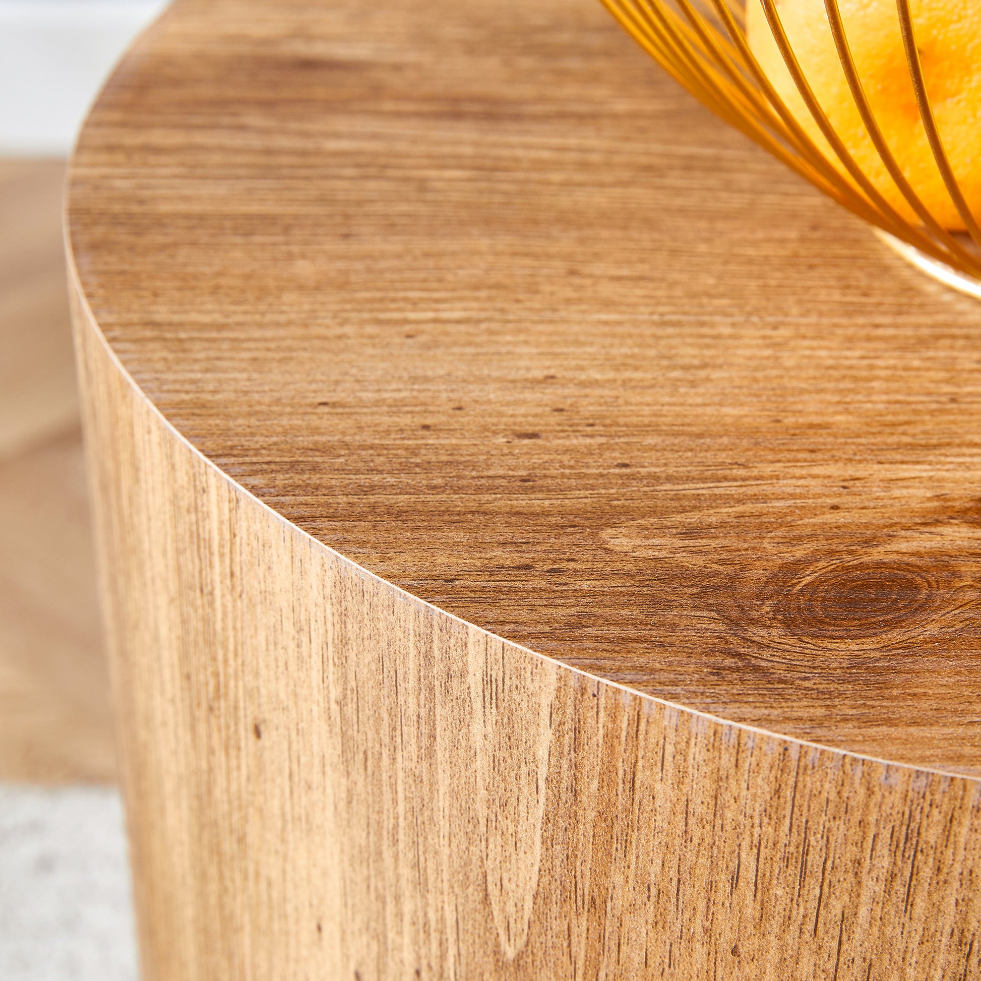 Round modern side table with wood grain finish and a gold fruit bowl on top