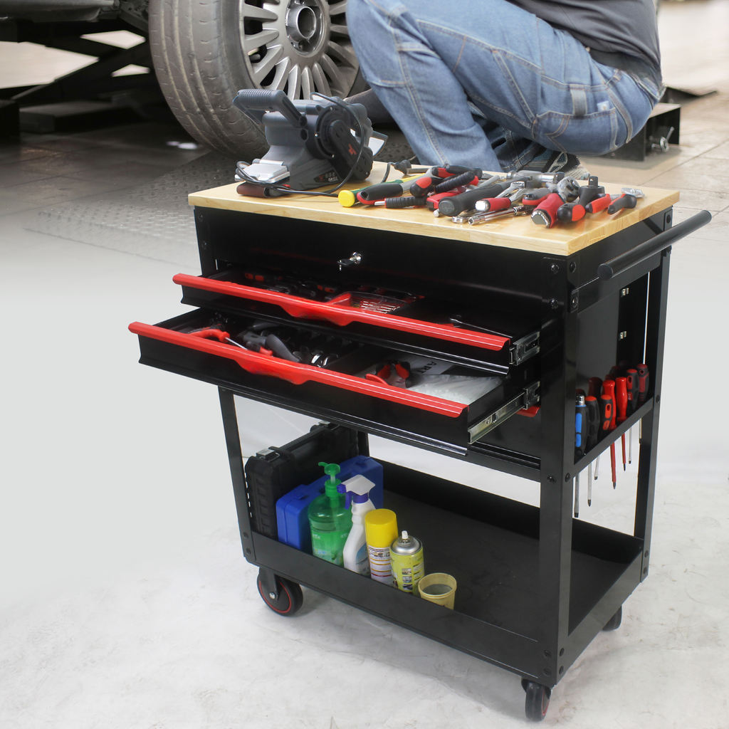 Black metal rolling tool chest with red drawer pulls and a wooden top stocked with tools