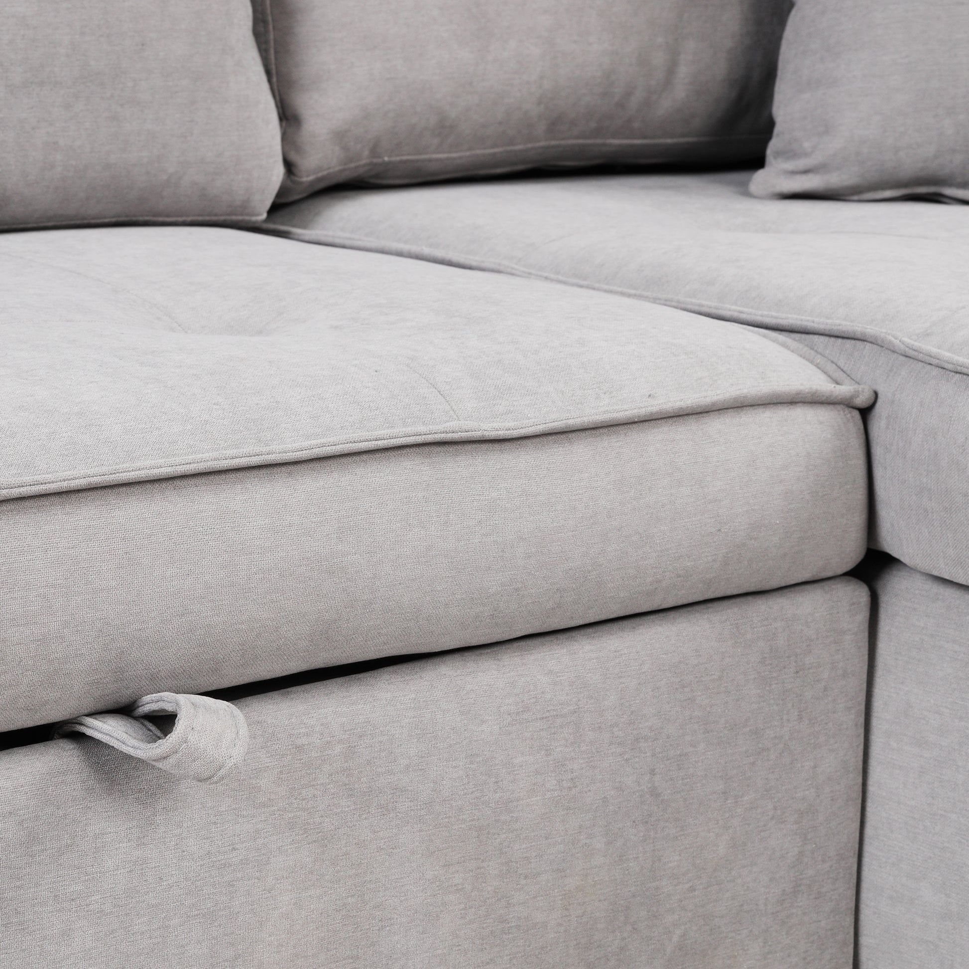 Closeup of a light grey linen fabric sectional sofa with tufted cushions and piping