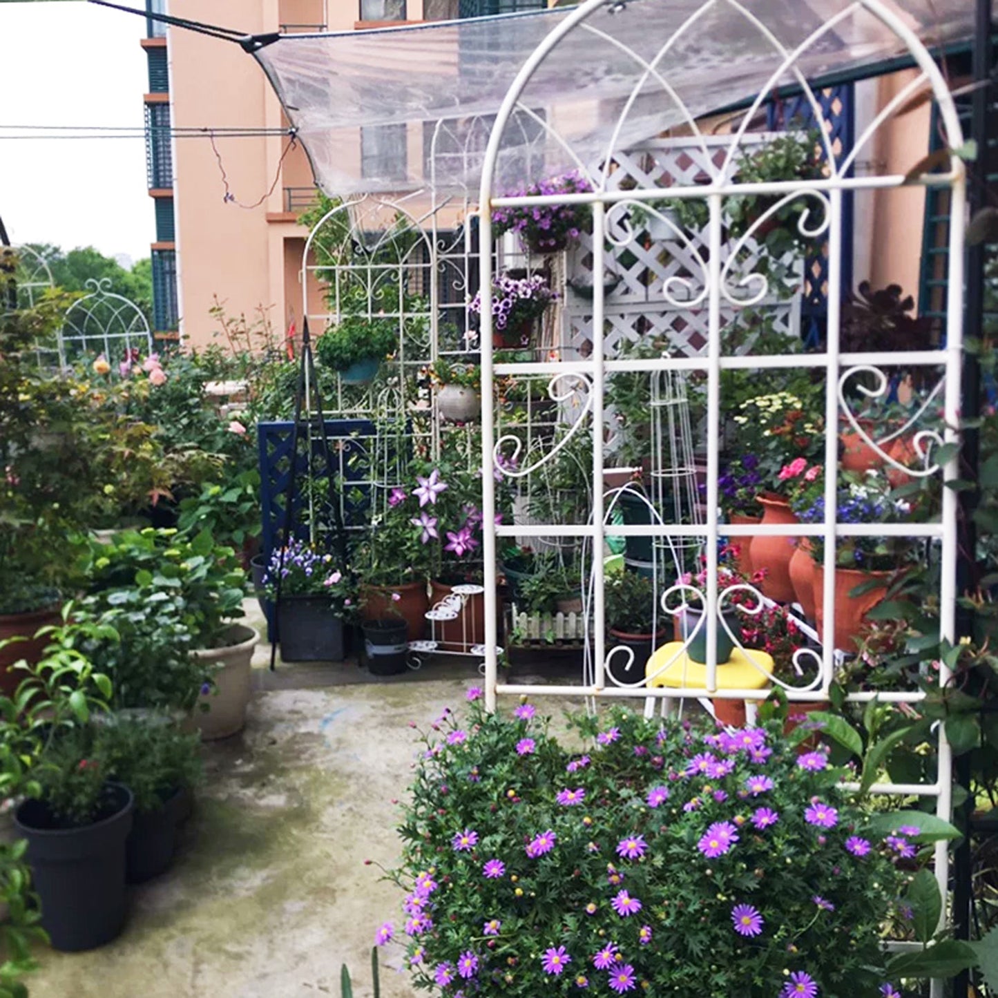 White ornate garden trellis with purple flowers and green plants