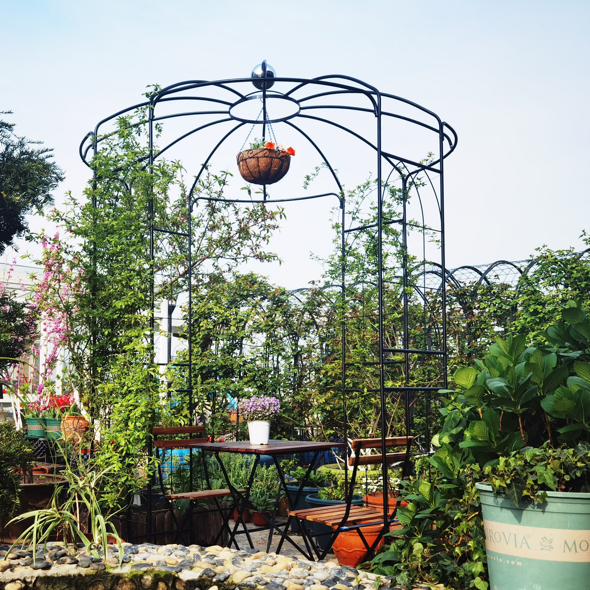 Black wrought iron garden arch with hanging basket and bistro set