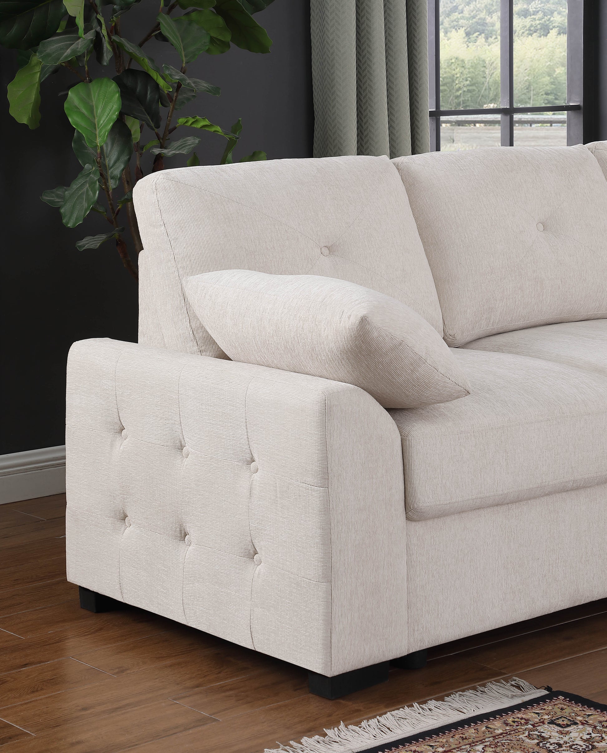 Closeup of a tufted beige sofa arm with a decorative throw pillow