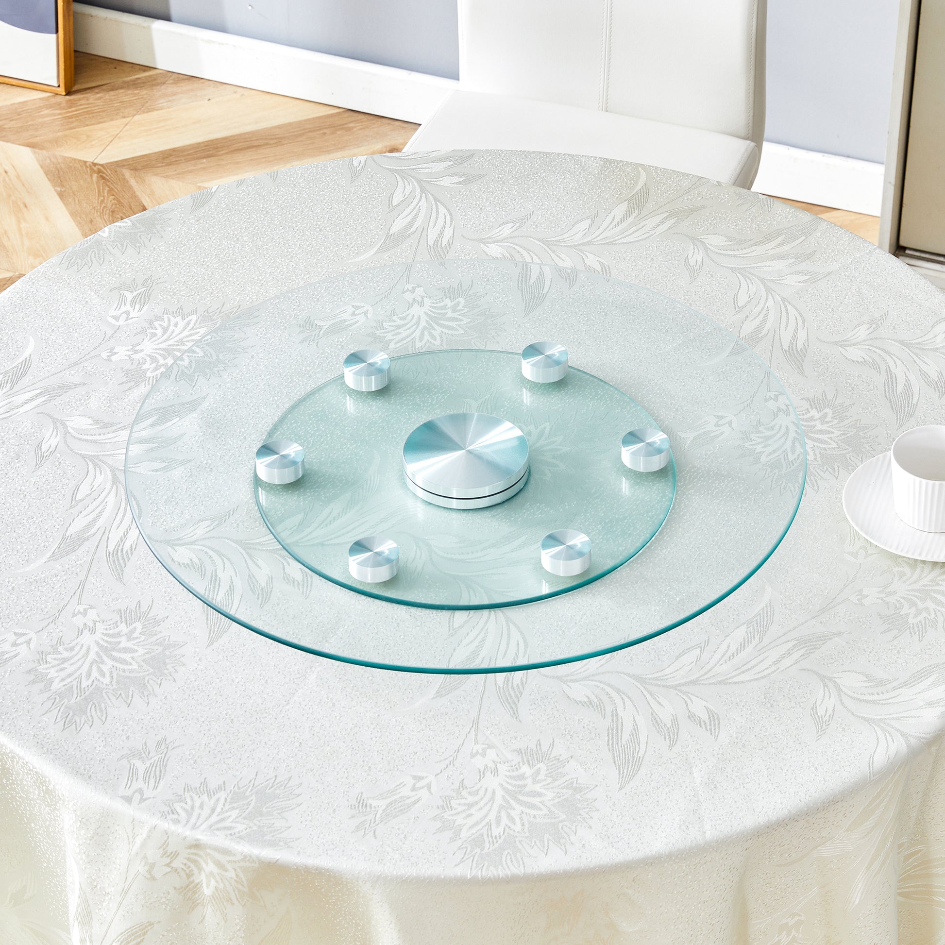 Glass lazy susan with chrome accents on a white floral tablecloth ideal for dining tables