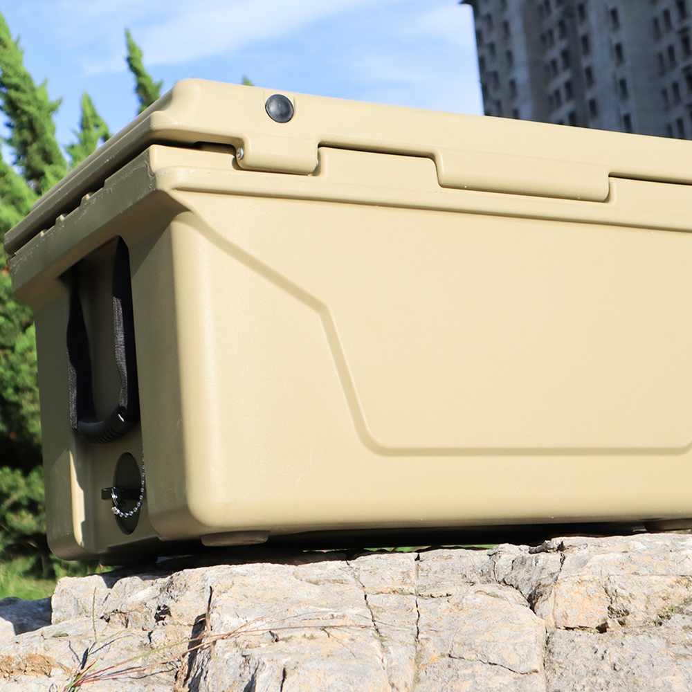 Tan rotomolded cooler with reinforced handles and drain plug on rocks