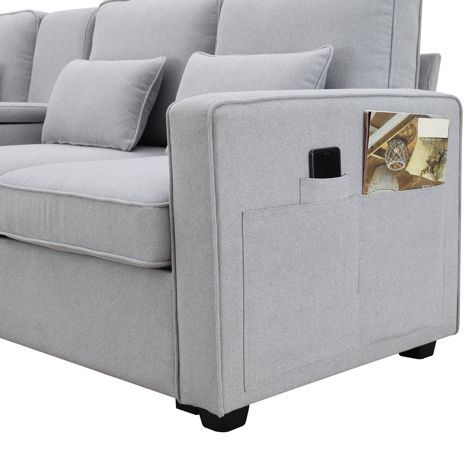 Light grey fabric sectional sofa with armrest pockets holding a phone and magazine