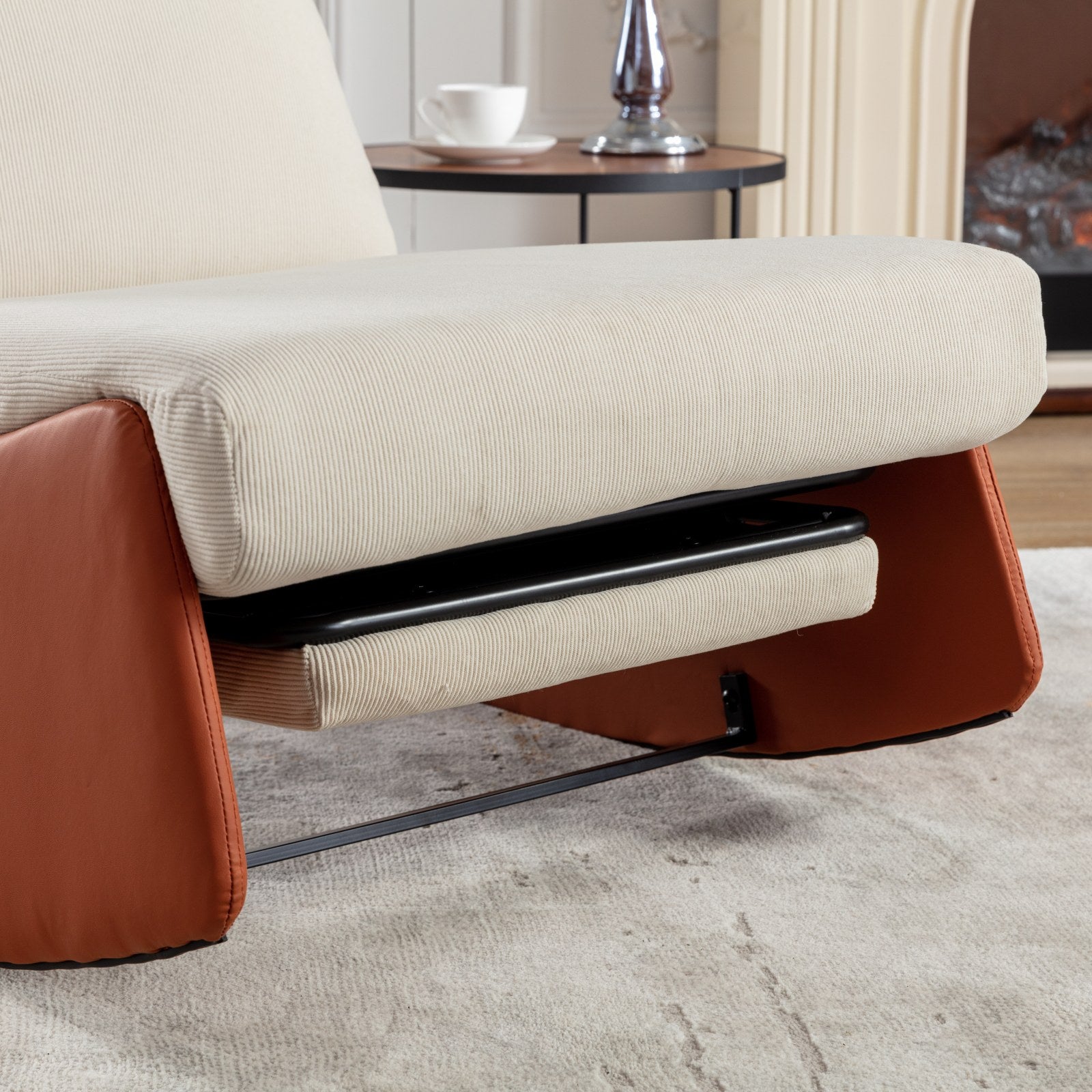 Closeup of a beige corduroy armchair with brown leather accents and a hidden footrest
