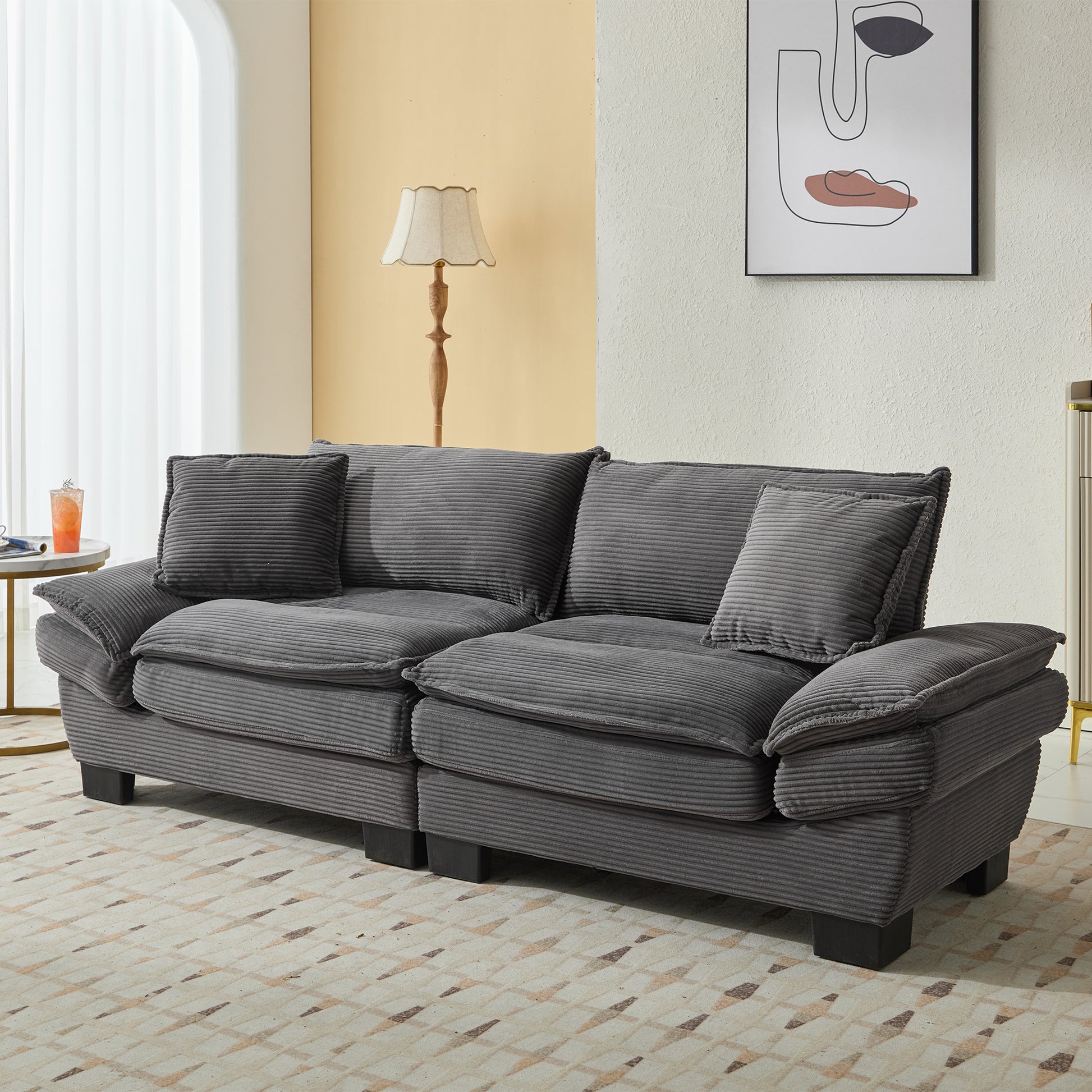 A charcoal gray corduroy sofa with plush cushions and matching throw pillows sits on a cream and beige geometric rug