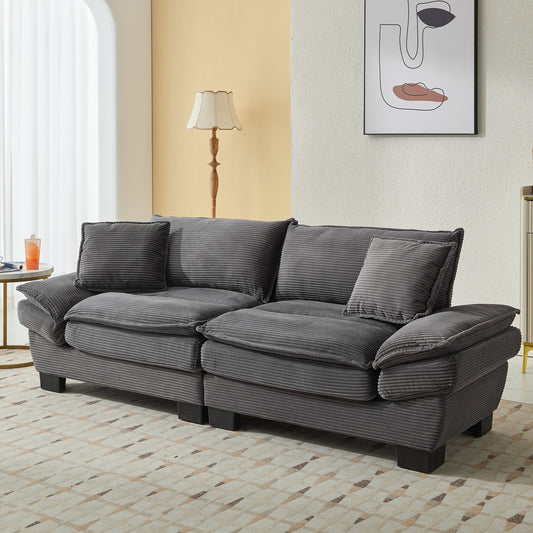 A charcoal gray corduroy sofa with plush cushions and matching throw pillows sits on a cream and beige geometric rug