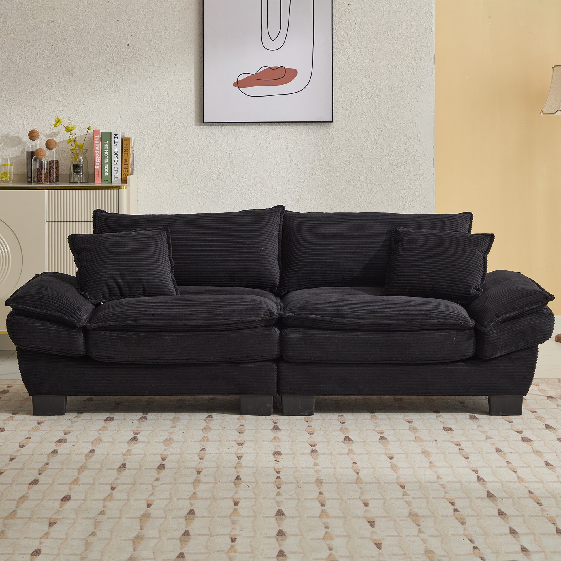 Black corduroy sofa with plush cushions and a minimalist abstract art print on the wall