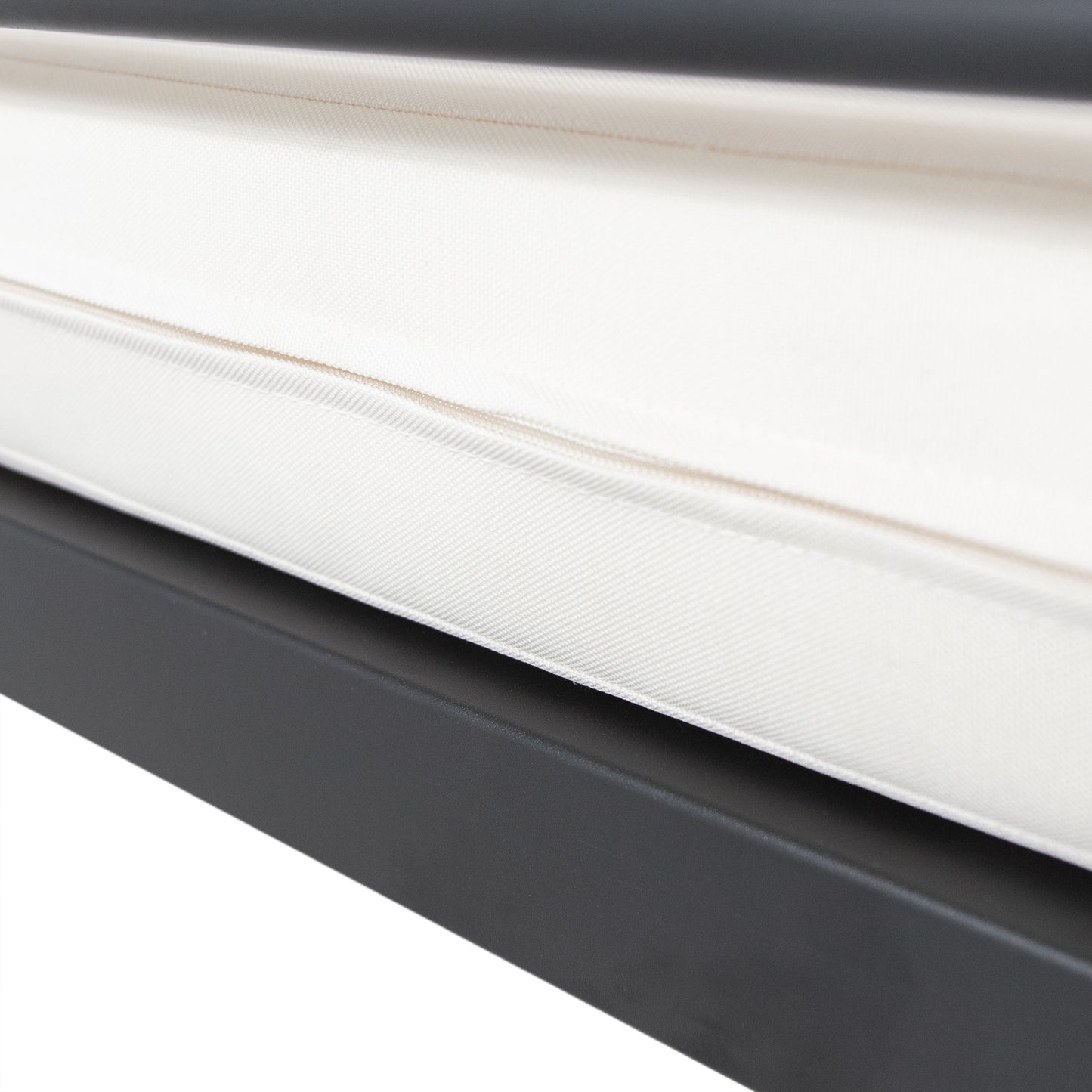 Closeup of a textured ivory outdoor cushion with a piped edge on a dark gray frame