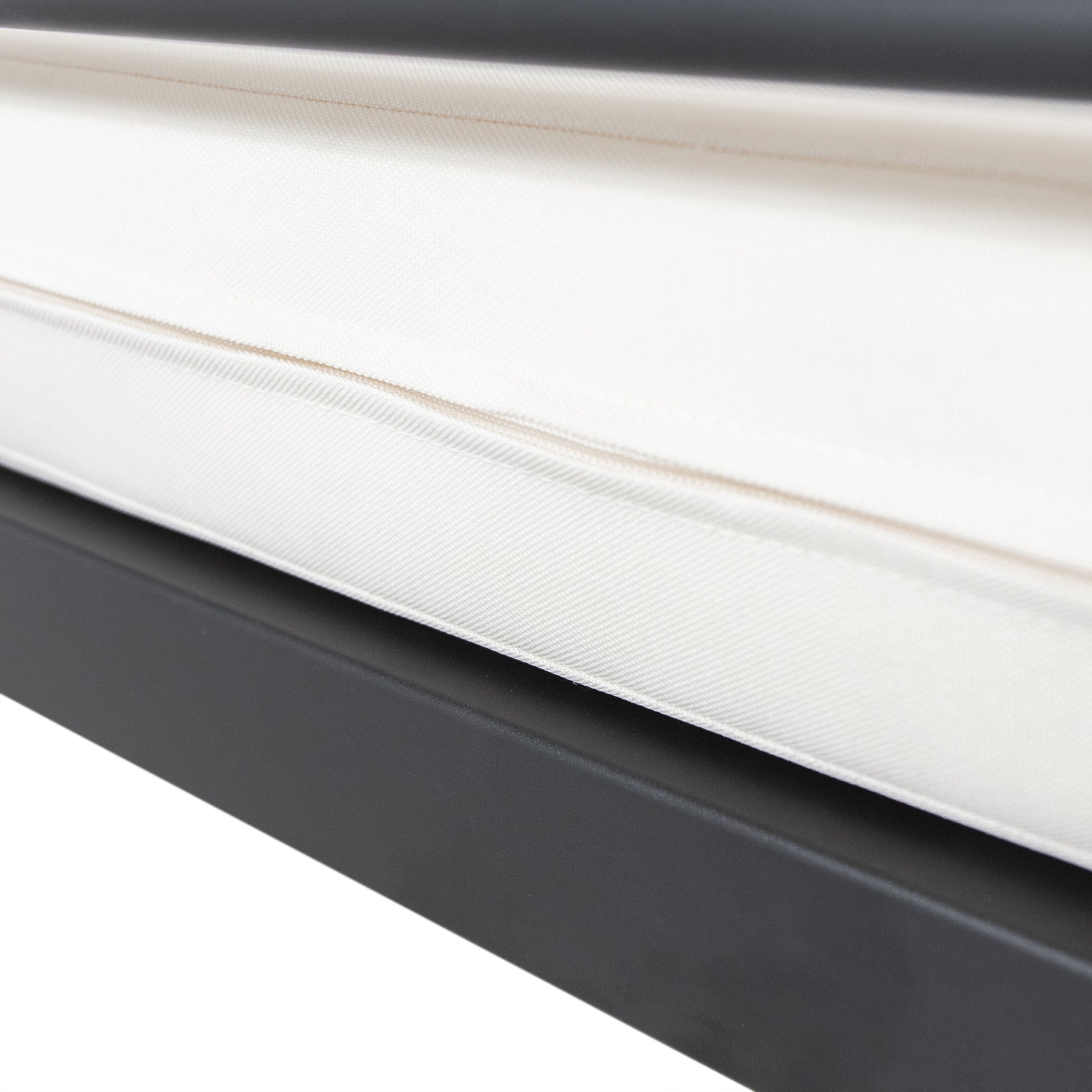 Closeup of a textured ivory outdoor cushion with a piped edge on a dark gray frame