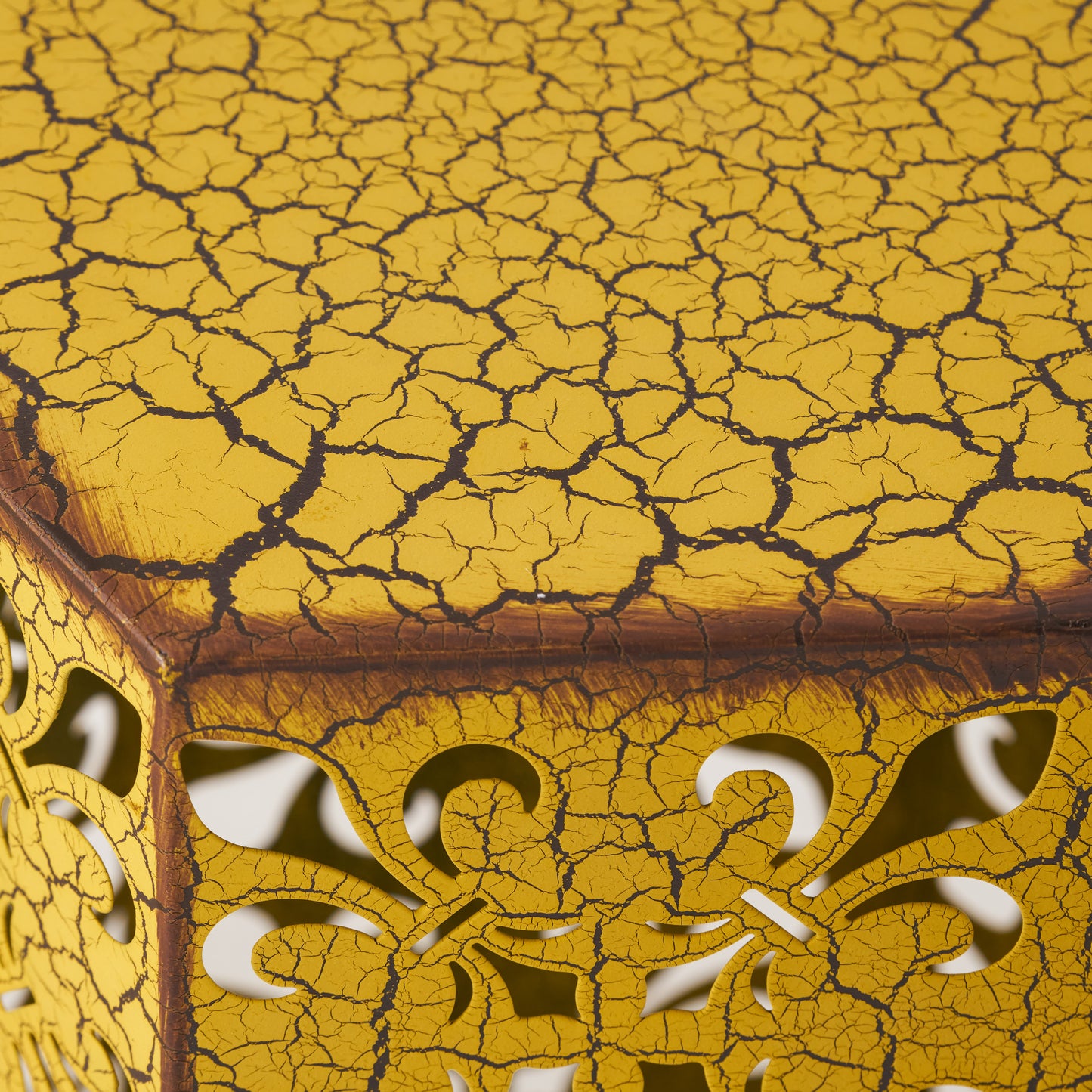 Yellow metal side table with intricate fleurdelis cutouts and distressed crackle finish