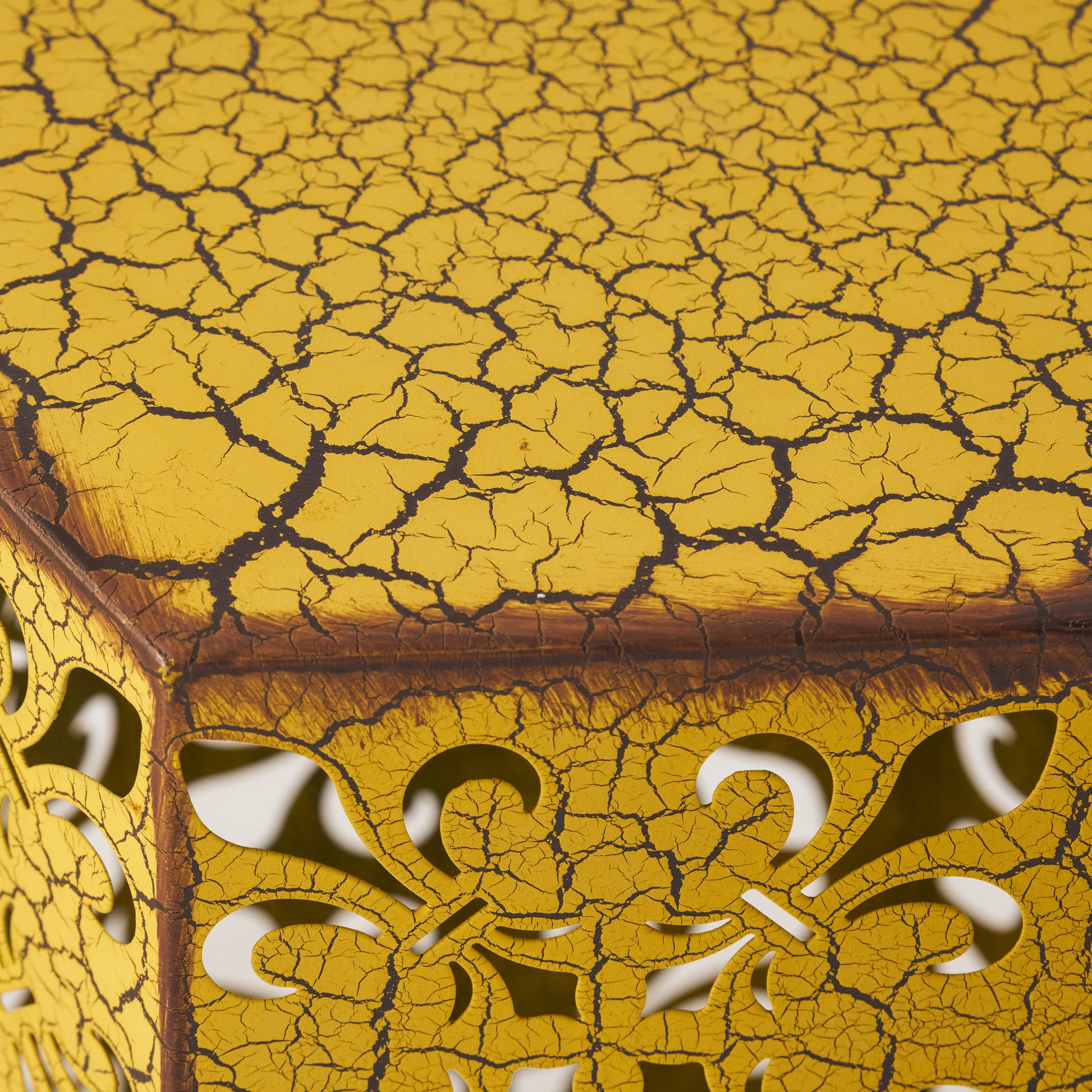 Yellow metal side table with intricate fleurdelis cutouts and distressed crackle finish