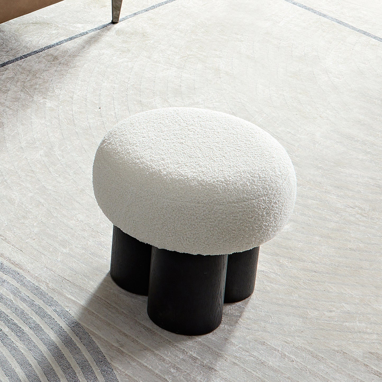 White boucle ottoman with three black wooden legs a contemporary accent stool