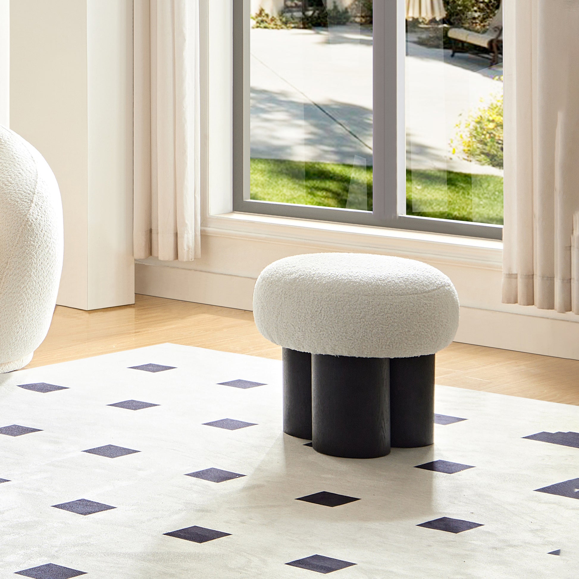 Plush ivory boucle ottoman with three dark wood cylindrical legs on a diamond pattern rug