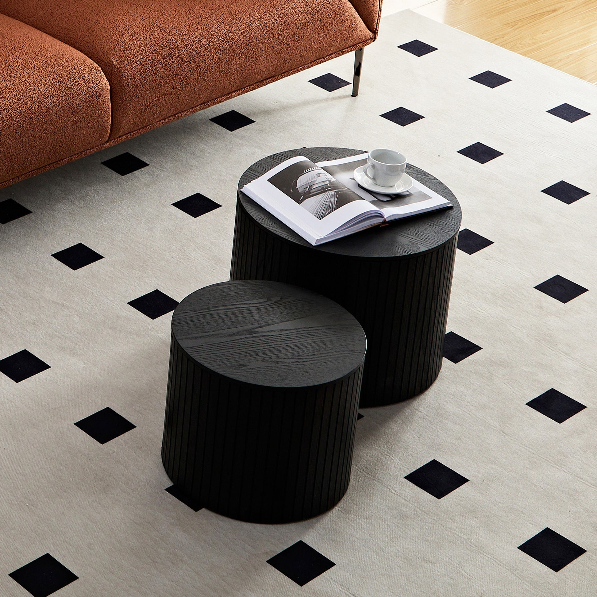 Set of two fluted black wood nesting side tables one with a book and coffee cup