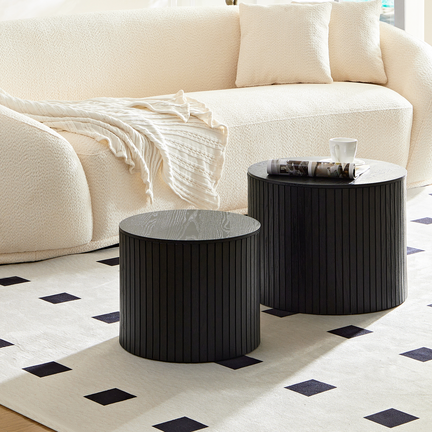 Two black fluted drum side tables with wood grain tops near a cream sofa
