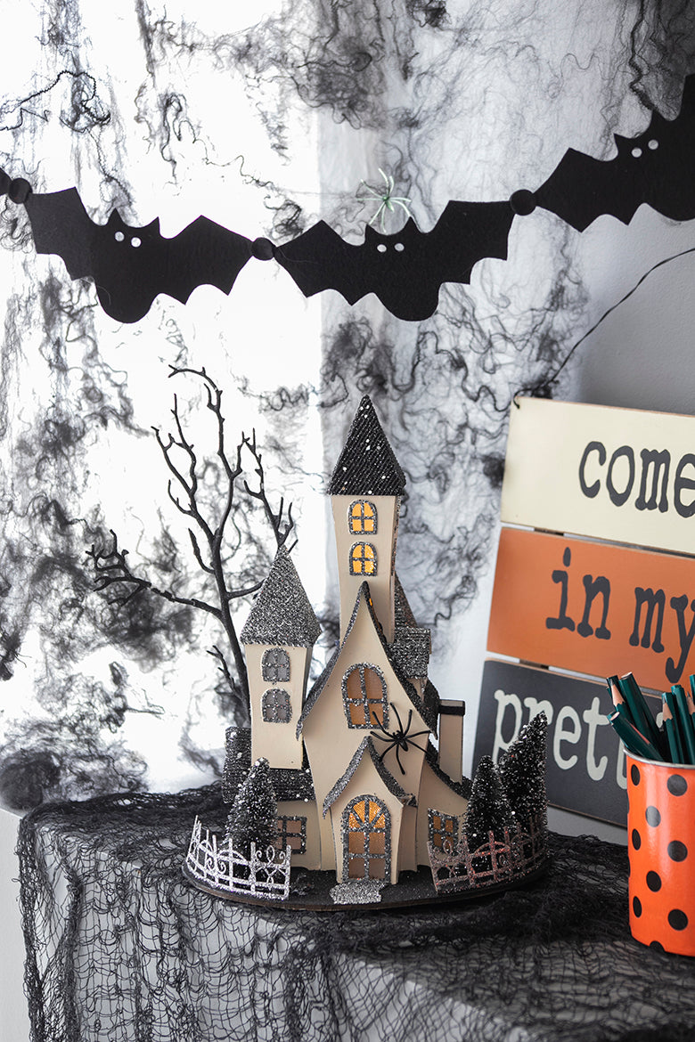Spooky haunted house figurine with glowing windows and bat garland