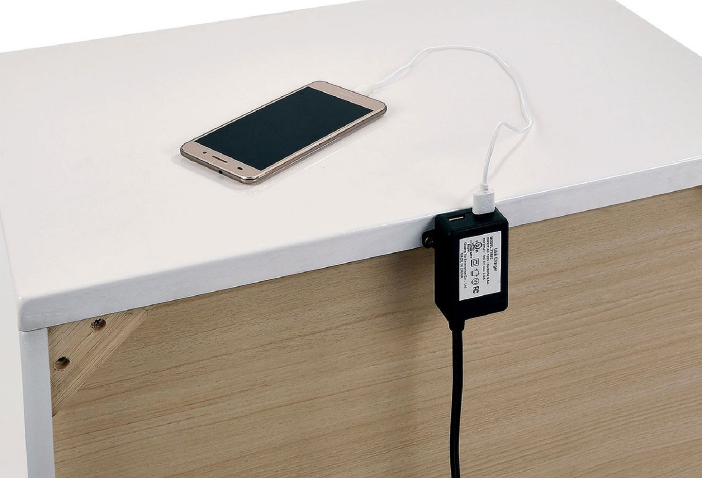 Gold smartphone charging via USB adapter clipped to a white furniture edge