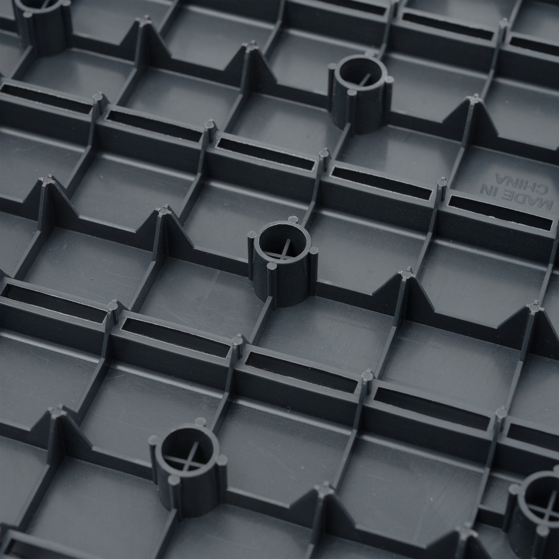 Dark gray interlocking floor tile base with raised grid pattern and circular supports