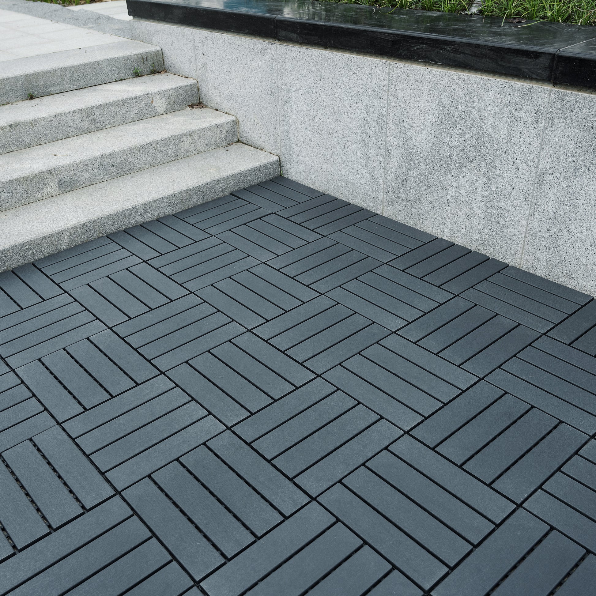 Dark grey interlocking composite decking tiles laid in a herringbone pattern