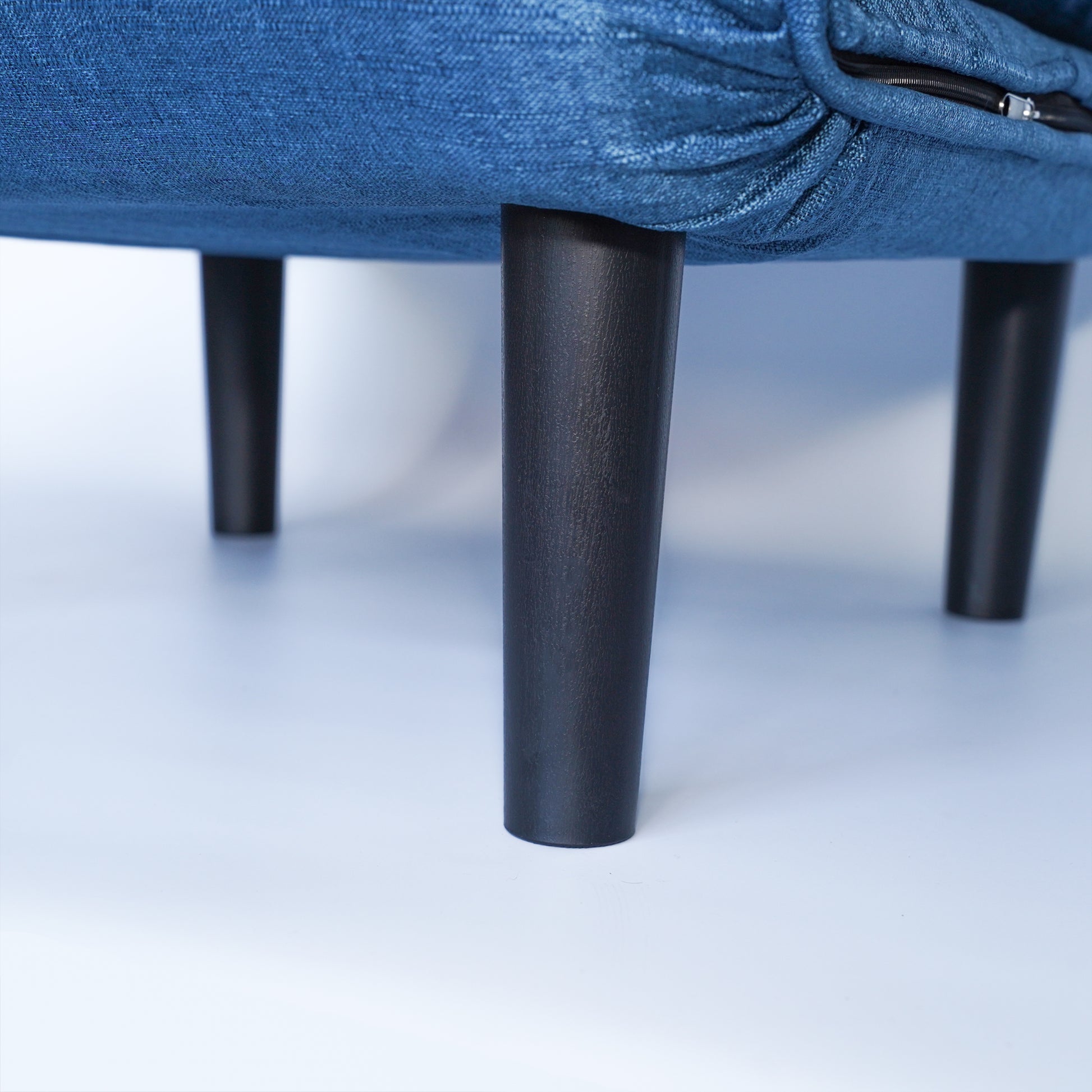 Closeup of dark wooden legs supporting a blue denim upholstered sofa