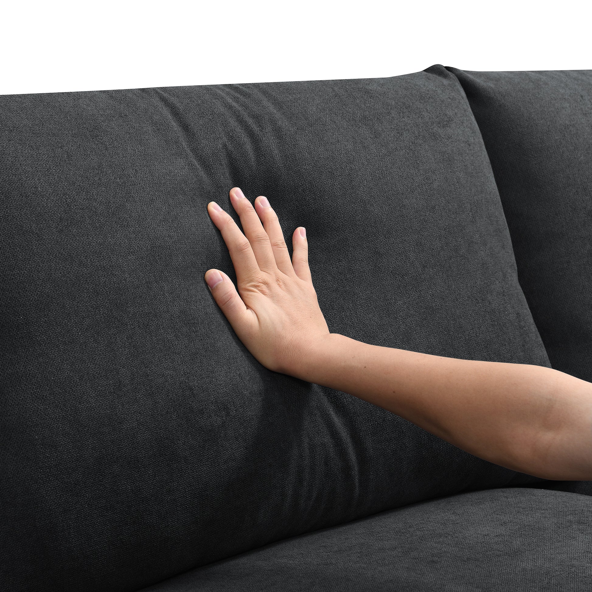 Hand pressing dark gray textured fabric sofa cushion demonstrating softness