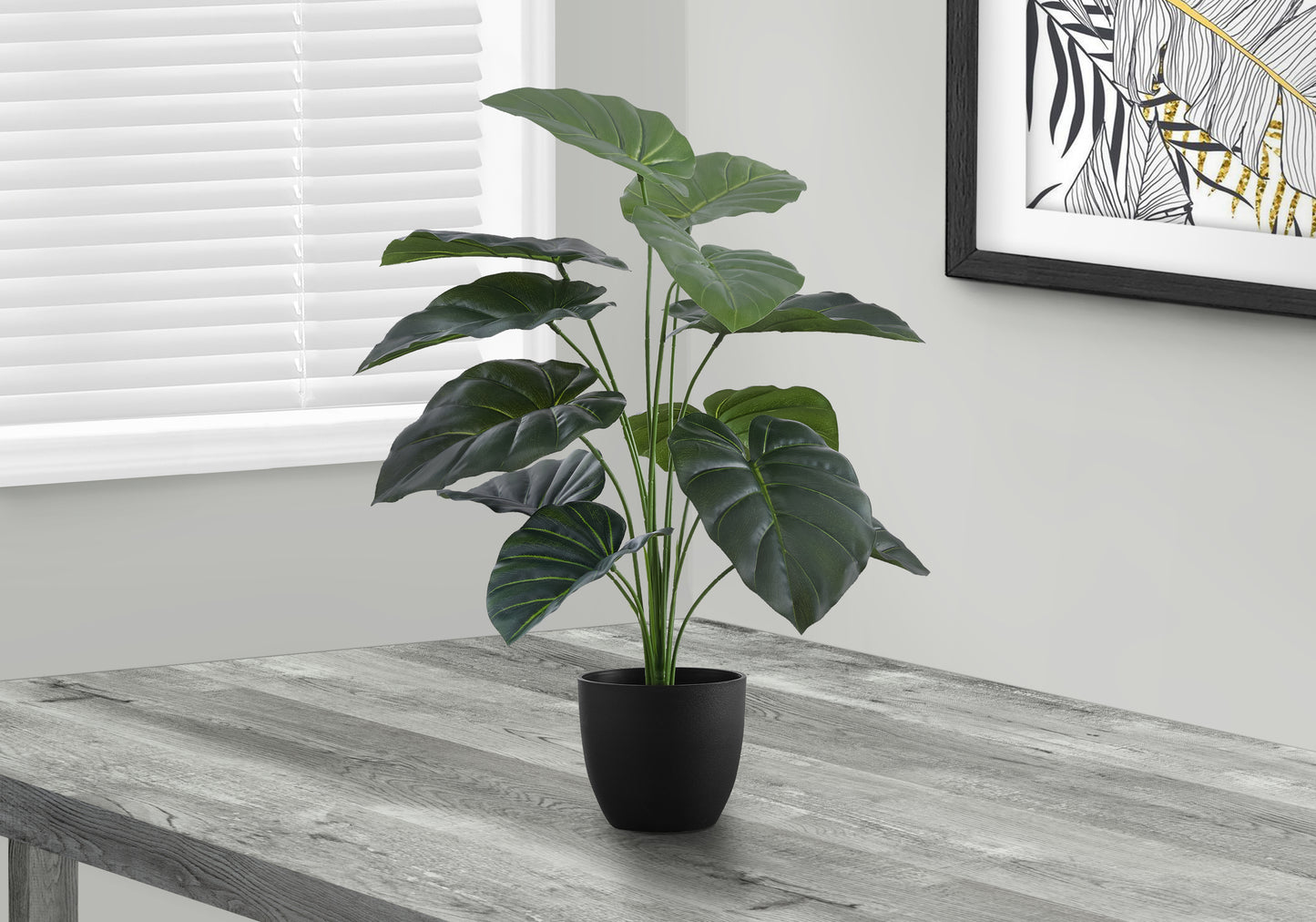 Large artificial plant with dark green leaves in a black pot on a gray wooden table