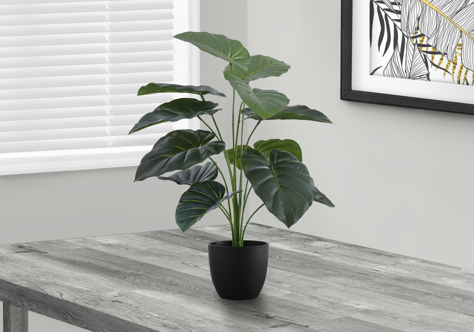 Large artificial plant with dark green leaves in a black pot on a gray wooden table
